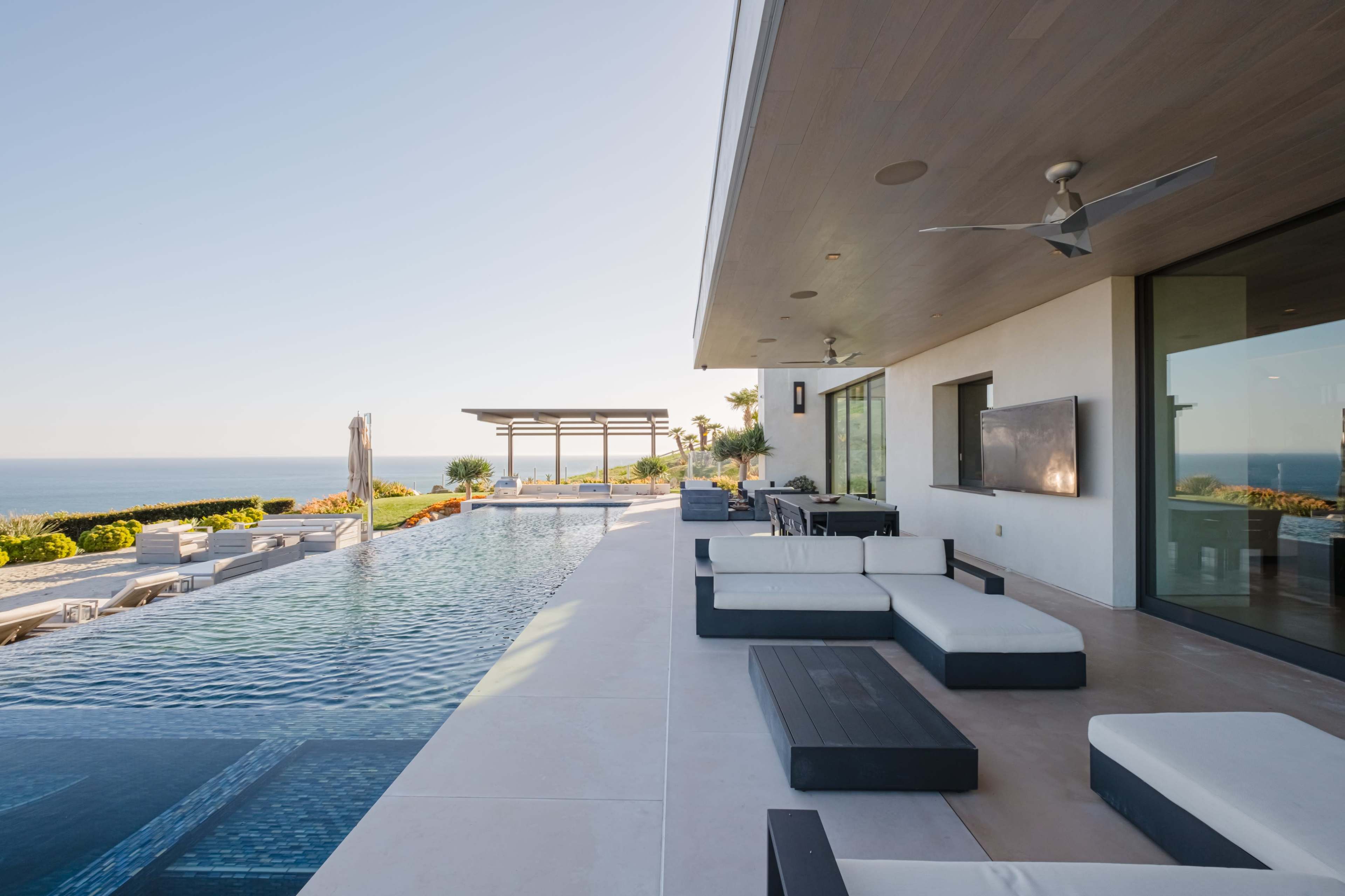 A modern outdoor space features a swimming pool, lounge seating, and a view of the ocean.