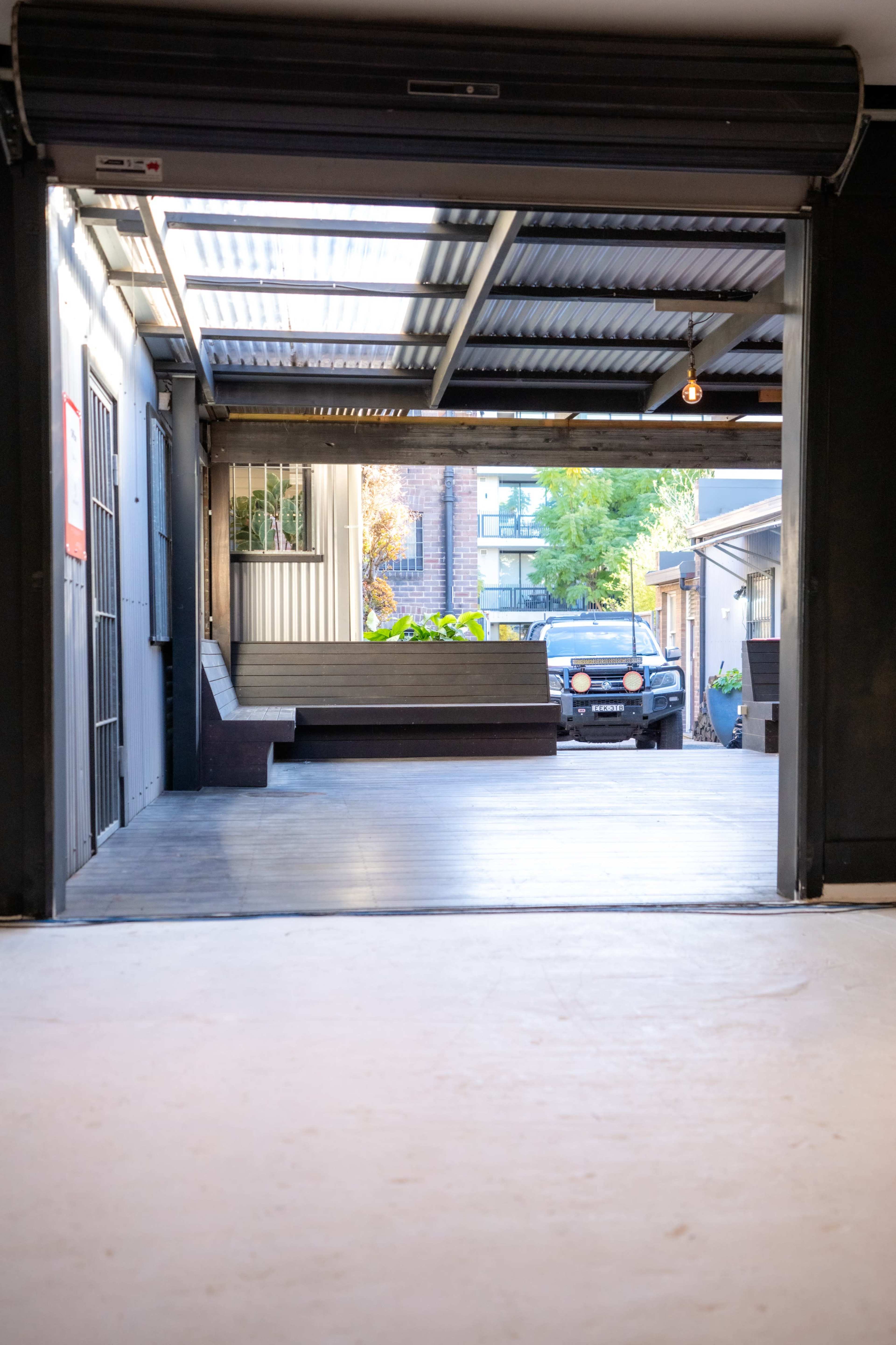 A space with an open garage door leading to a wooden deck area and a parked vehicle outside.