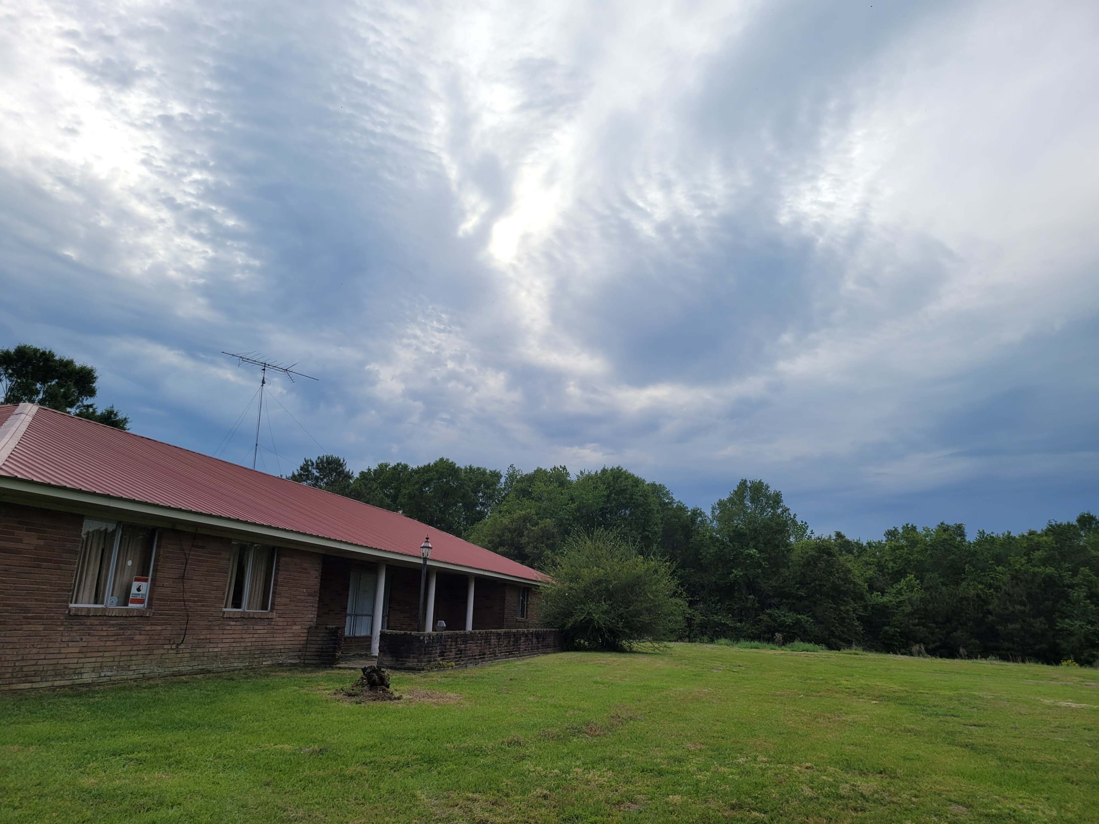 A brick house with a red roof sits on a grassy lot under a cloudy sky.