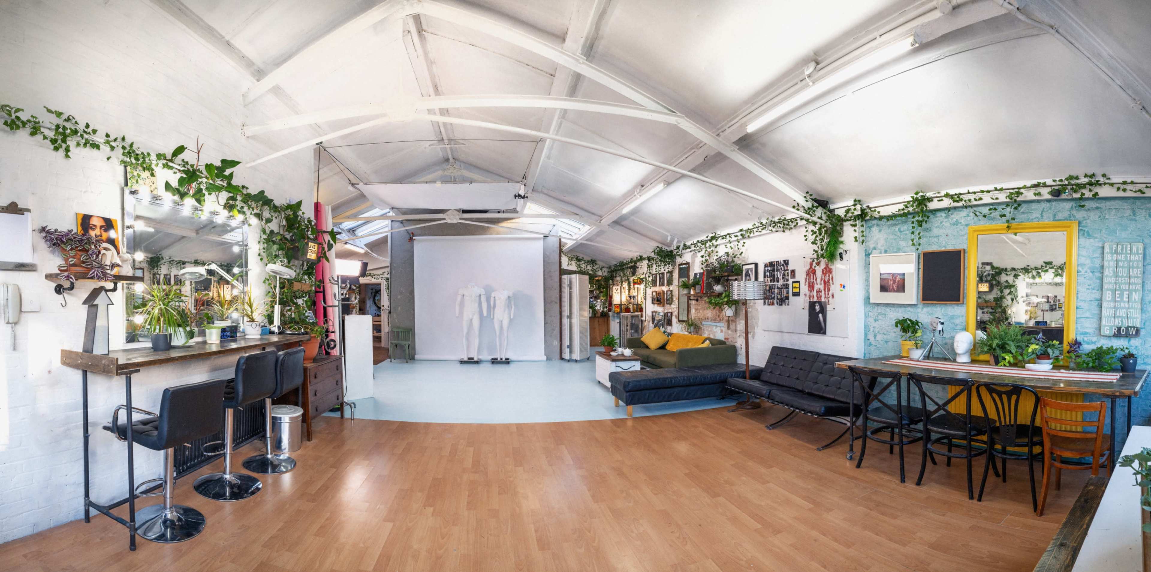 A spacious, well-lit studio with plants, various artworks, a seating area, and large mirrors.
