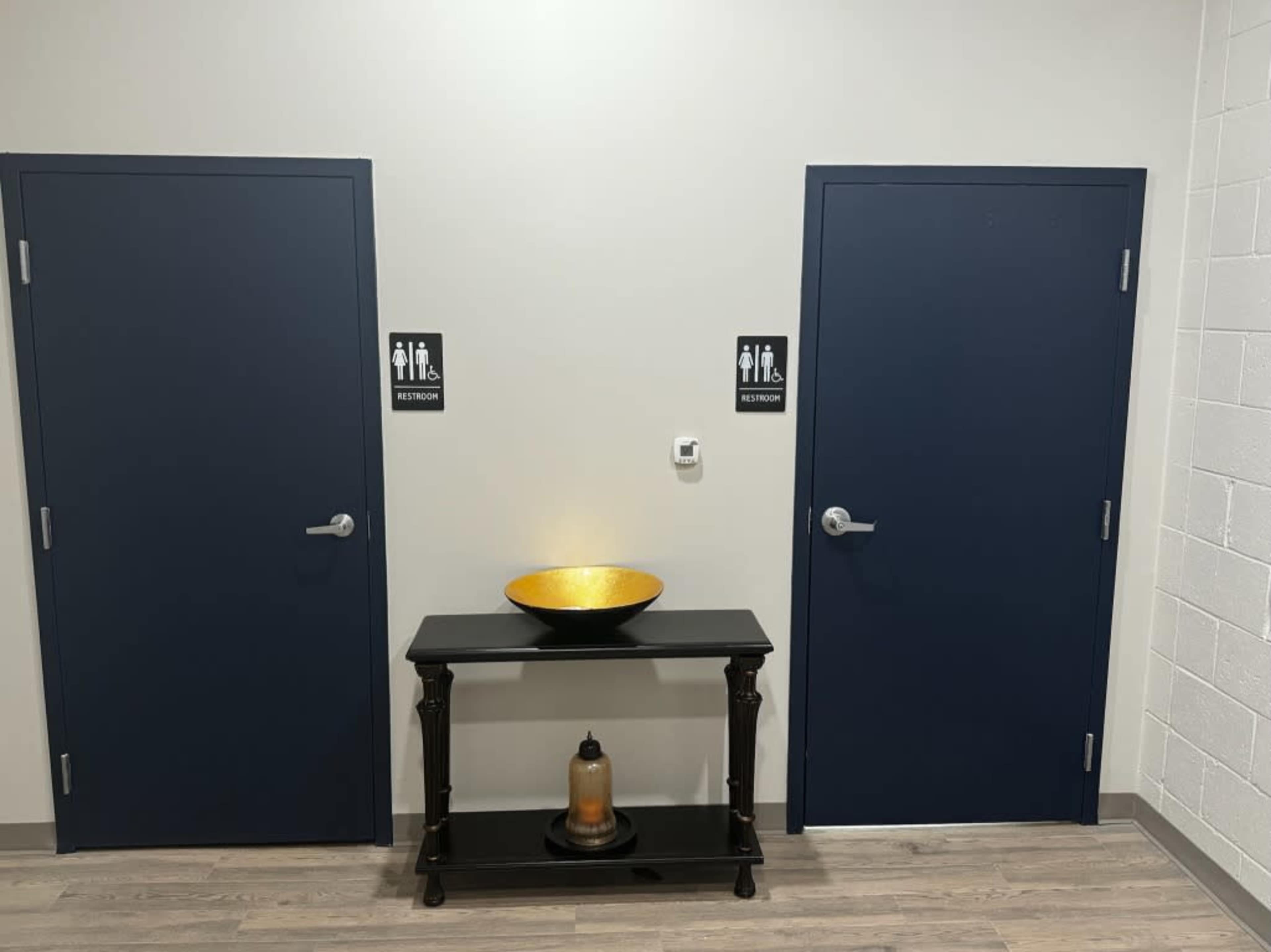 Two blue doors labeled with restroom signs, situated on either side of a black table adorned with a decorative bowl and a small candle holder.