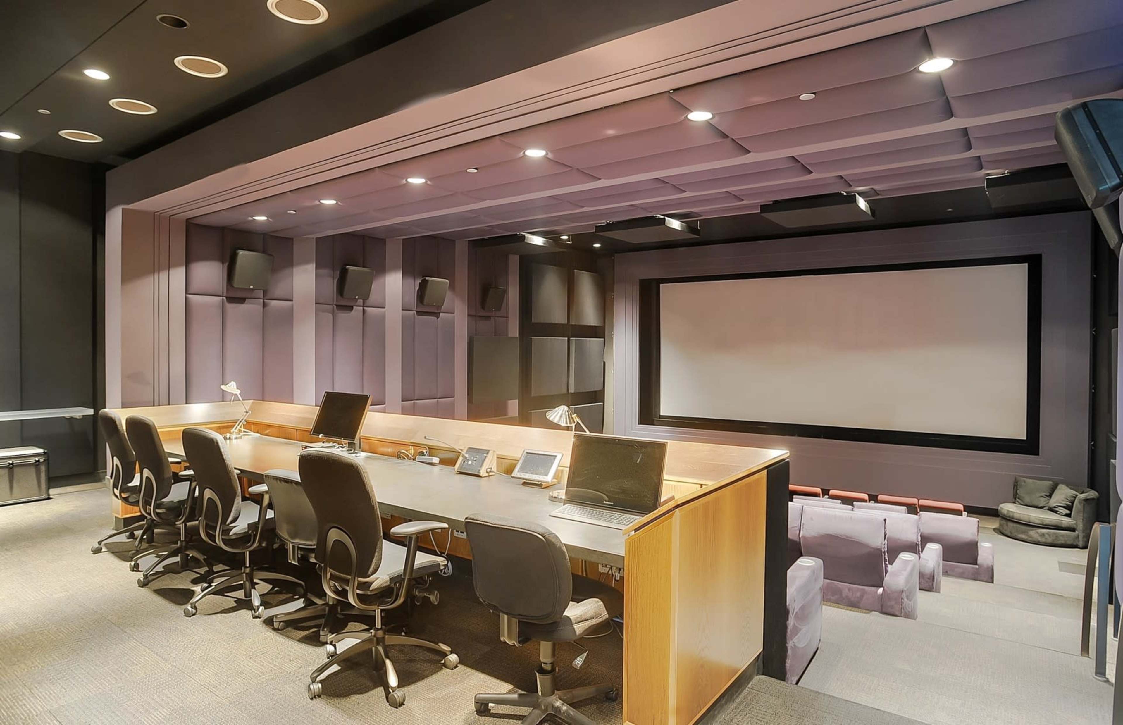 A multimedia control room with a large screen at the front and a long desk equipped with monitors and chairs for operators.