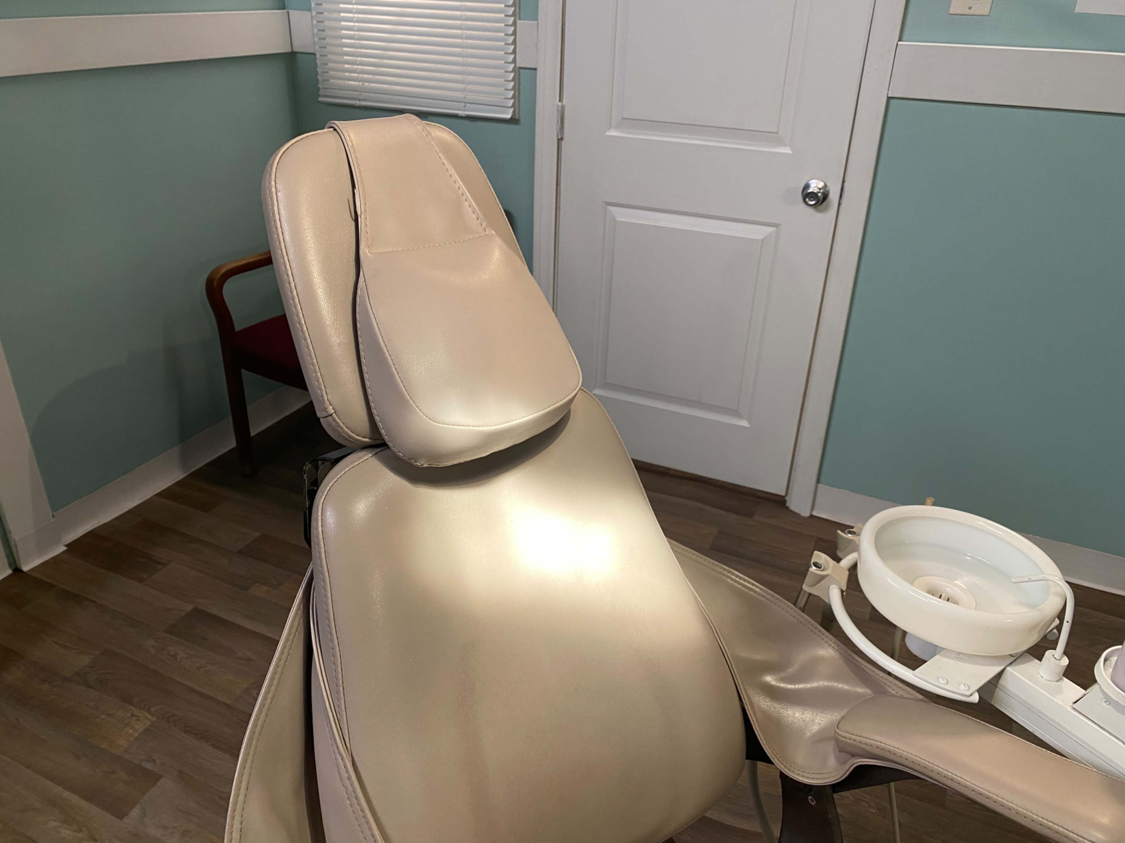 The image shows a dentist's examination chair positioned next to a white cabinet in a dental office.