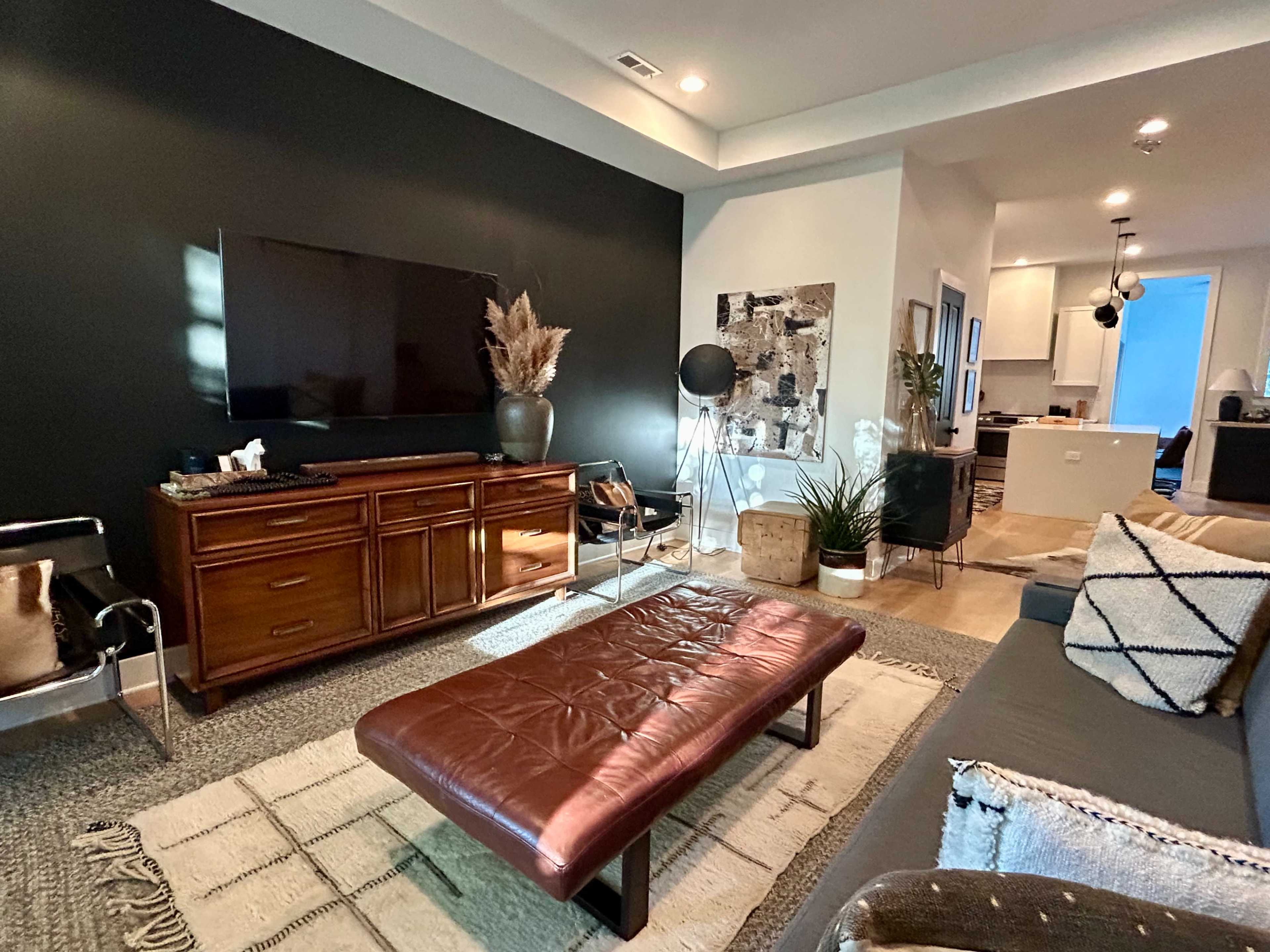 The image shows a modern living room with a dark accent wall, a brown leather coffee table, and an entertainment unit against the wall.