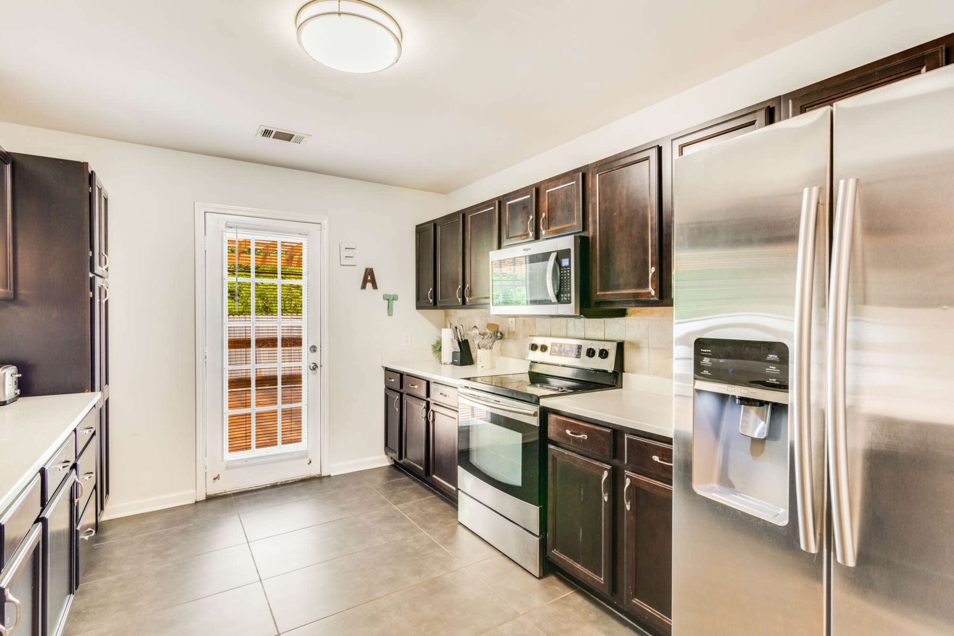 The kitchen features dark wooden cabinets, stainless steel appliances, and a door leading to an exterior patio.