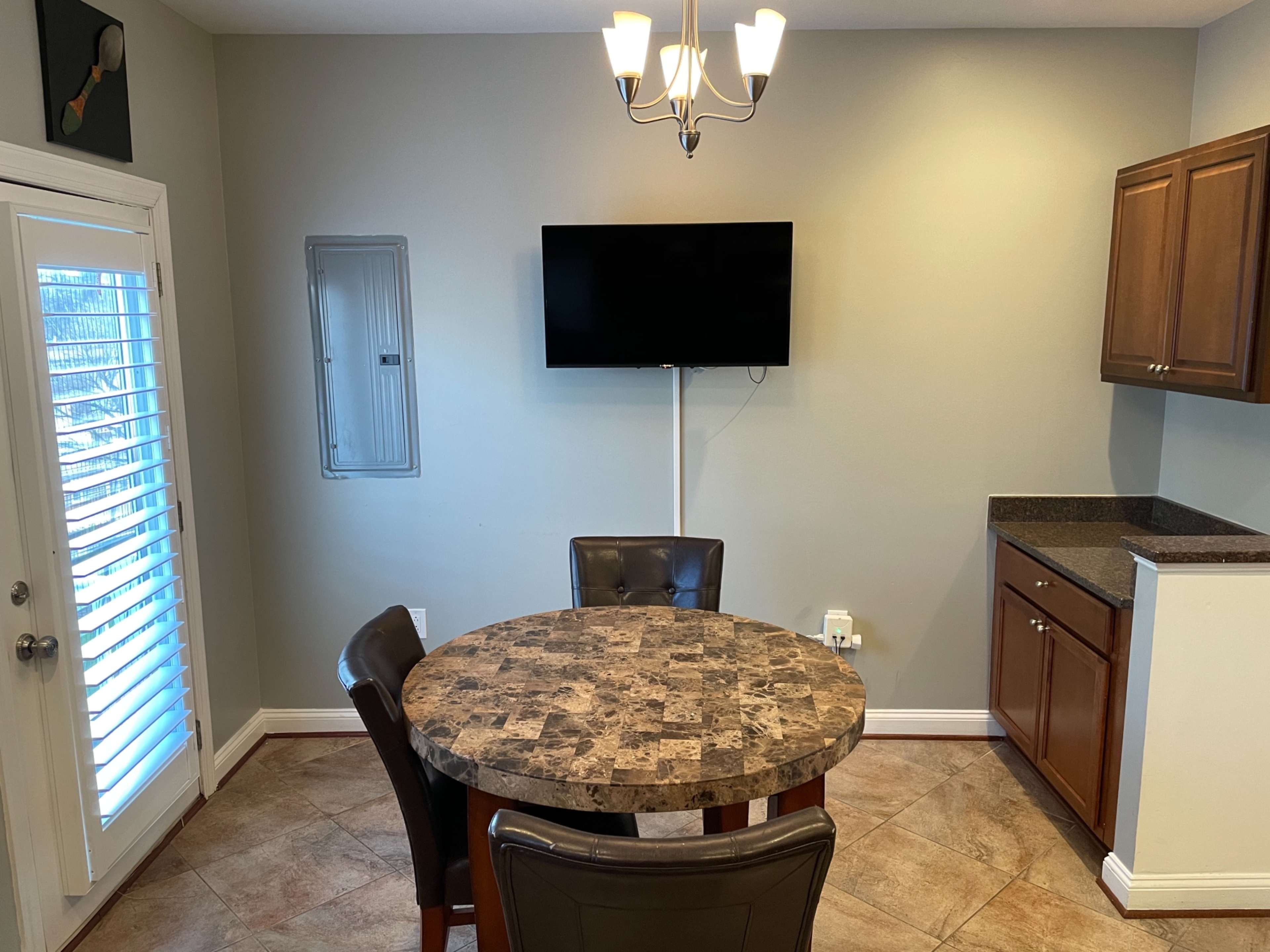 A small dining area with a round stone table, four chairs, a wall-mounted TV, and a cabinet in a kitchen setting.