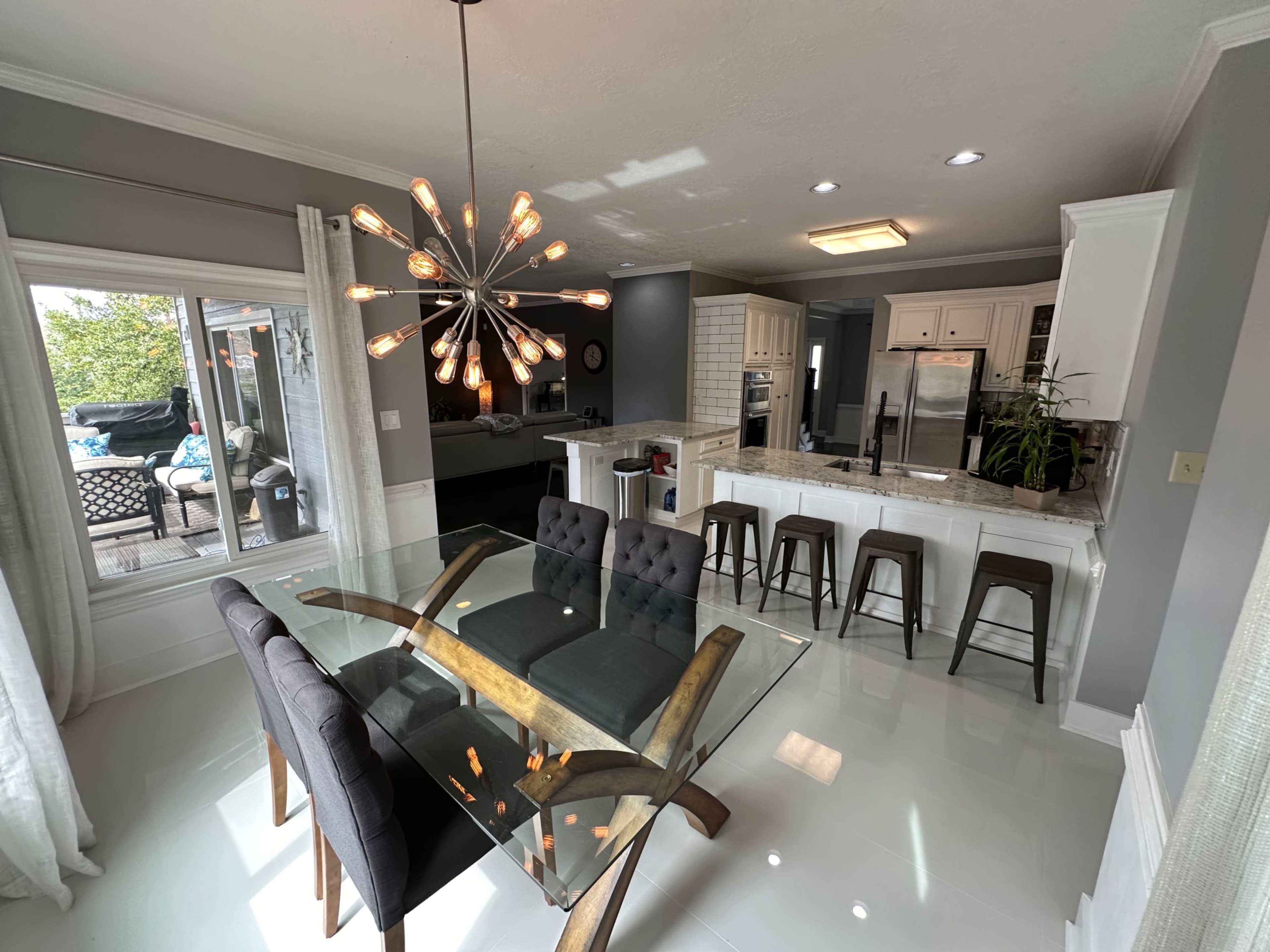 A modern kitchen features a glass dining table with upholstered chairs, a granite countertop, and stainless steel appliances.