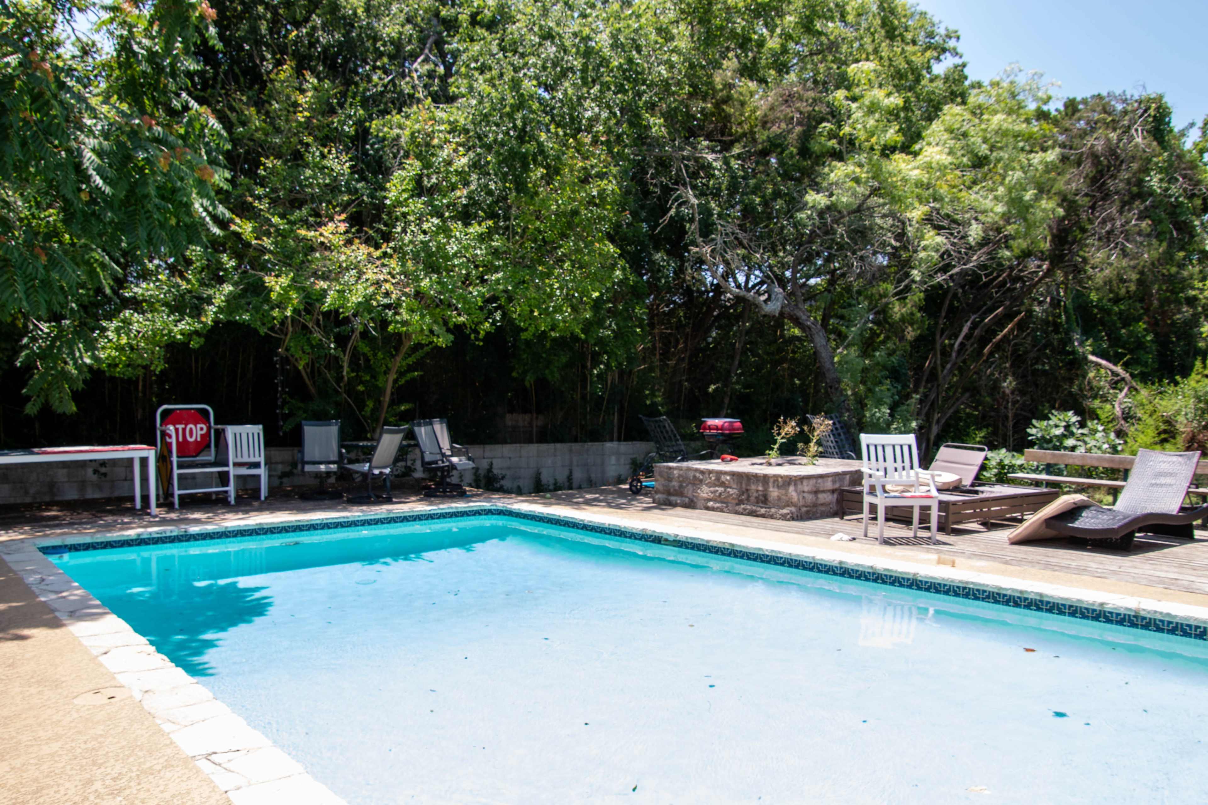 A rectangular pool is surrounded by lounge chairs and some trees, with a stop sign visible in the background.