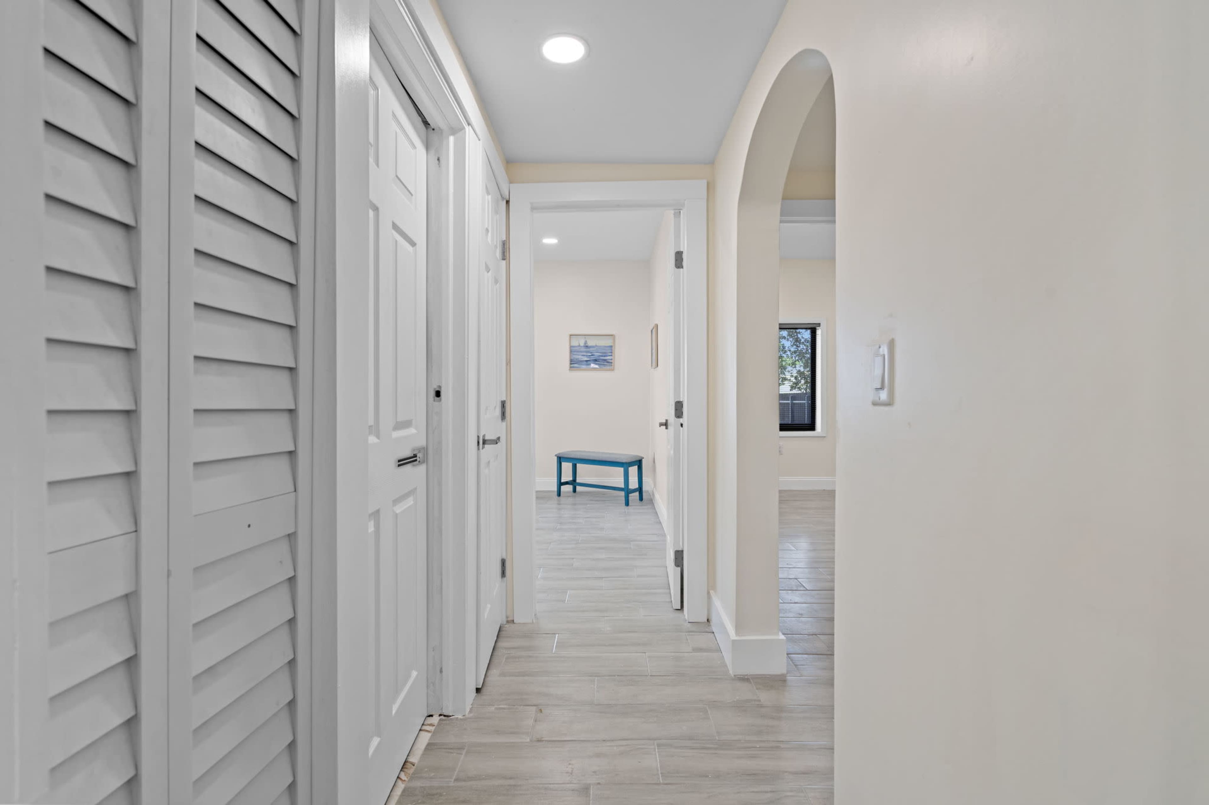 The hallway features white doors and a light-colored tiled floor with an arched doorway leading to a room at the end.