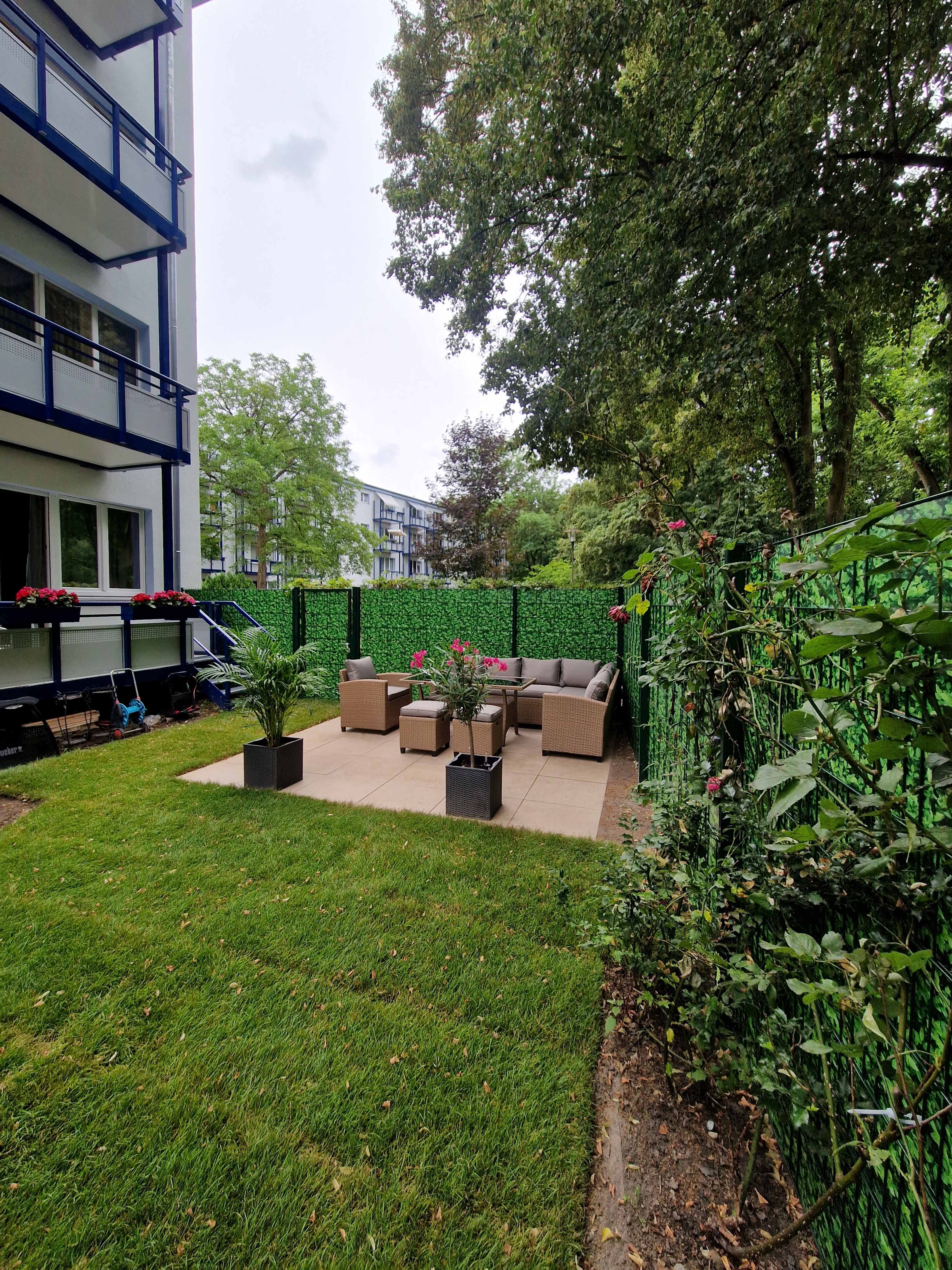 A patio area features a seating arrangement with beige furniture surrounded by greenery and a privacy screen.