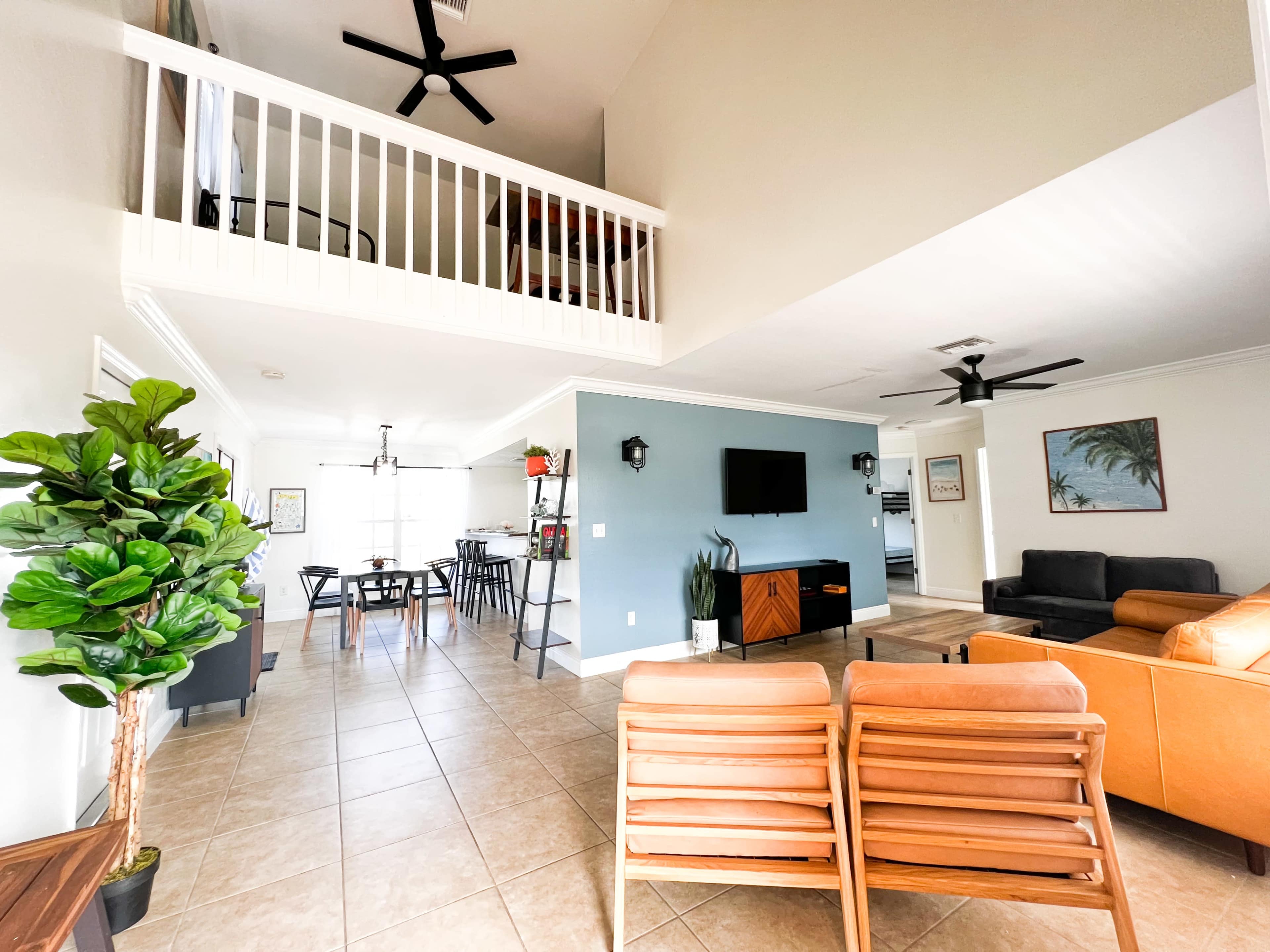 The interior of a spacious living area features a seating arrangement, a television, and a view of a dining space with a loft above.
