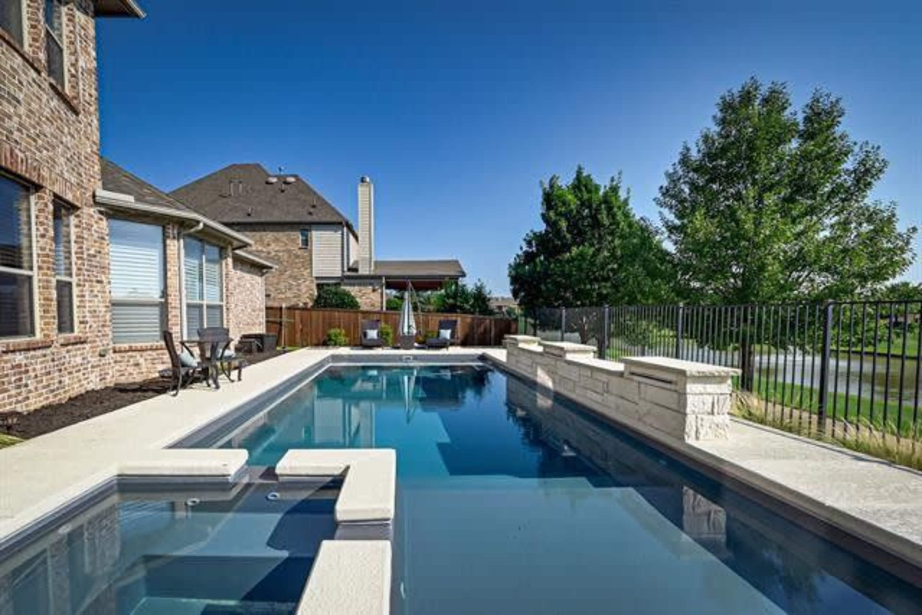 A residential backyard with a swimming pool surrounded by a stone patio and a wooden fence.
