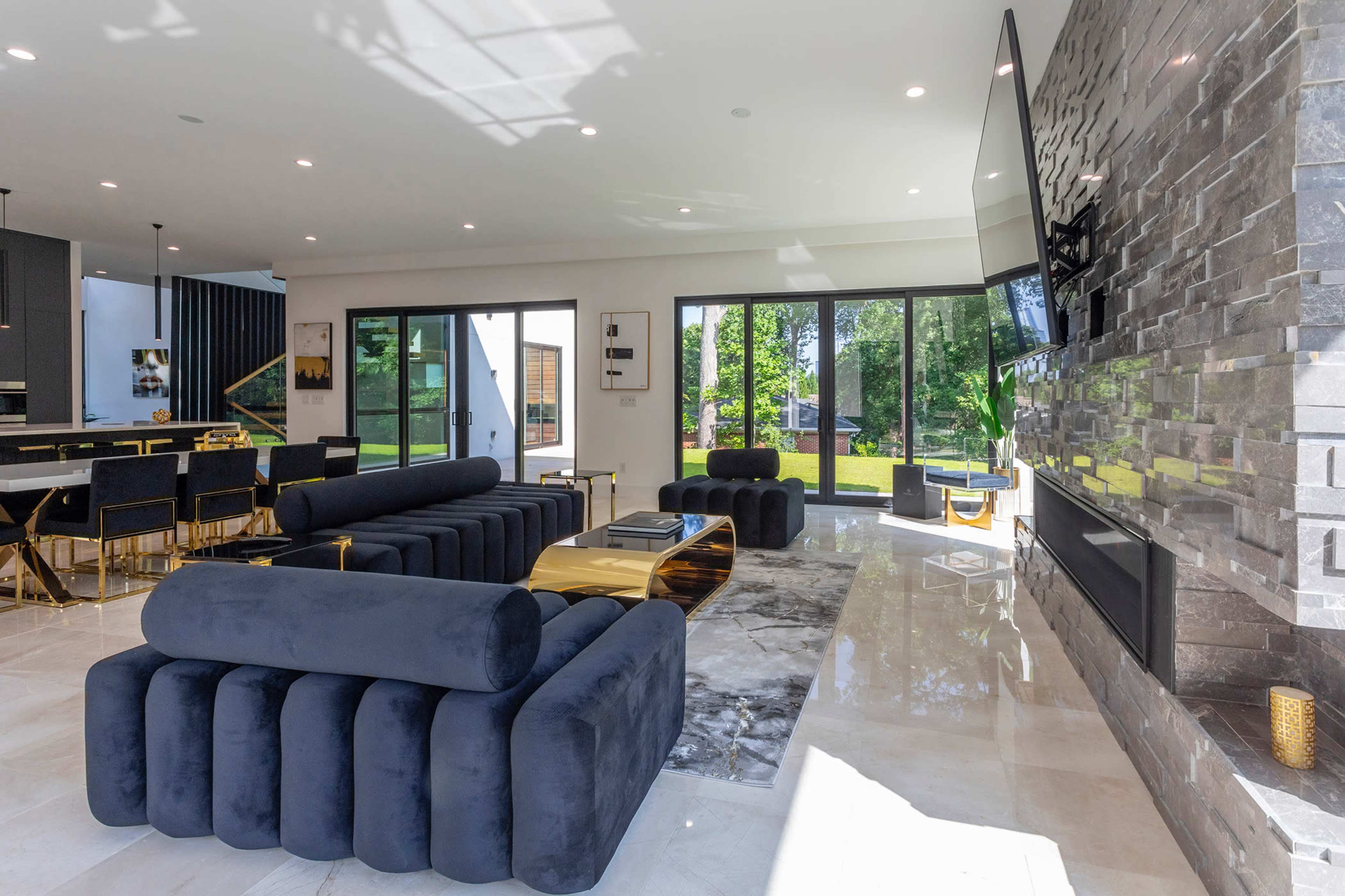 The image shows a modern living room featuring a black sectional sofa, a marble coffee table, and large glass doors leading to a garden outside.