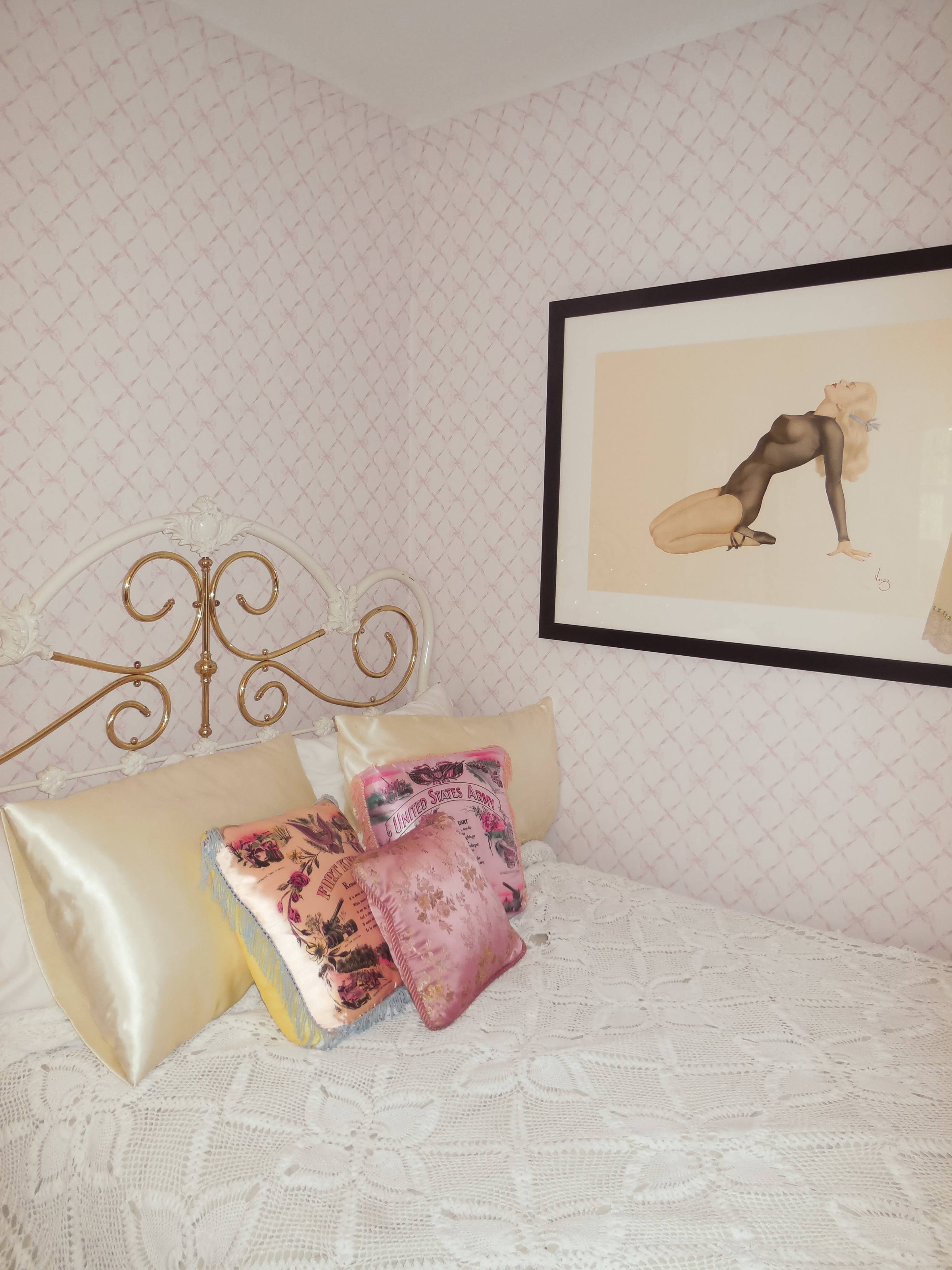 The image shows a corner of a bedroom with a bed adorned with decorative pillows and a framed artwork on the wall.