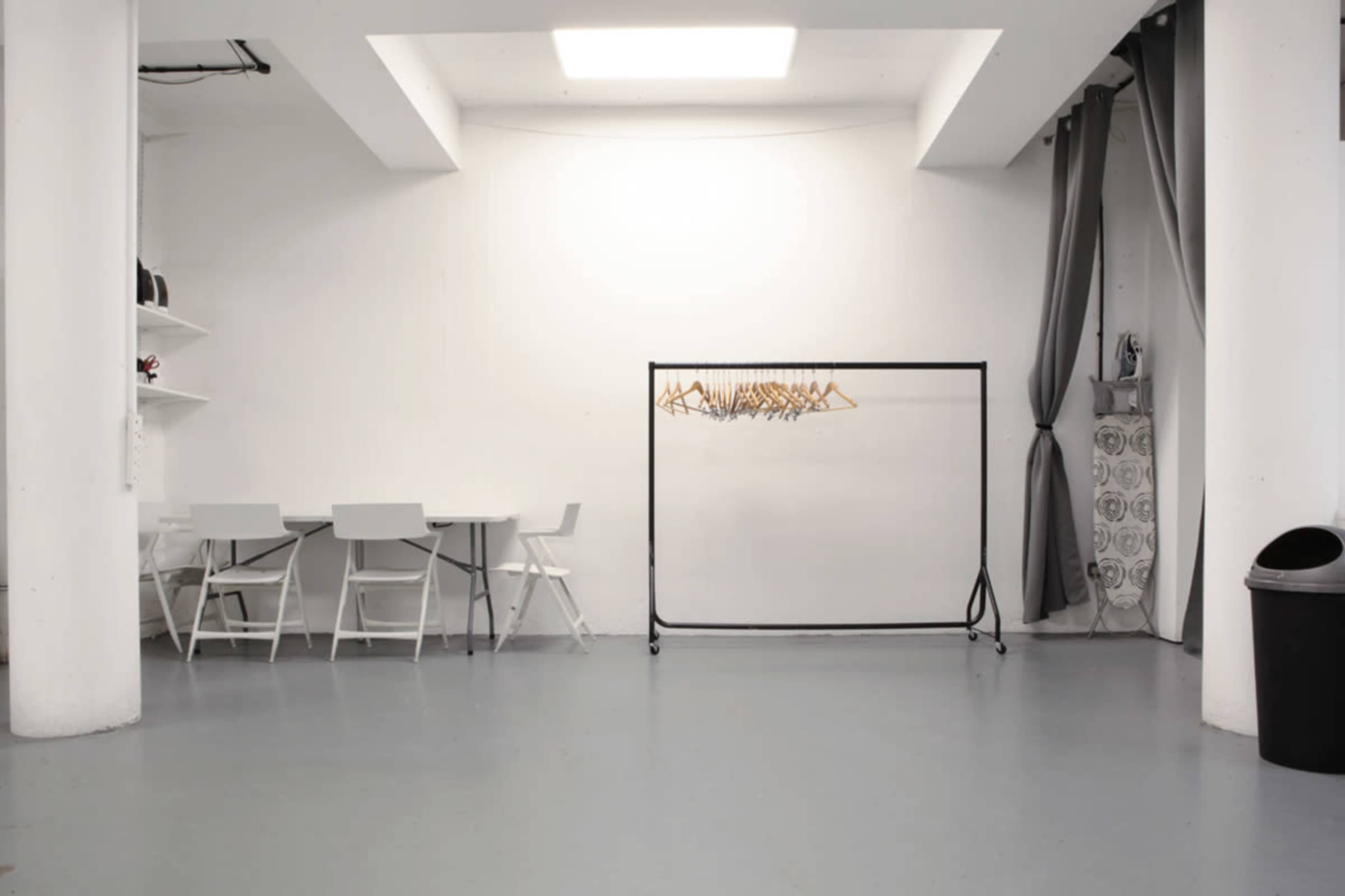 A minimalist room with a clothing rack in the center, a table with chairs on one side, and a trash bin in the corner.