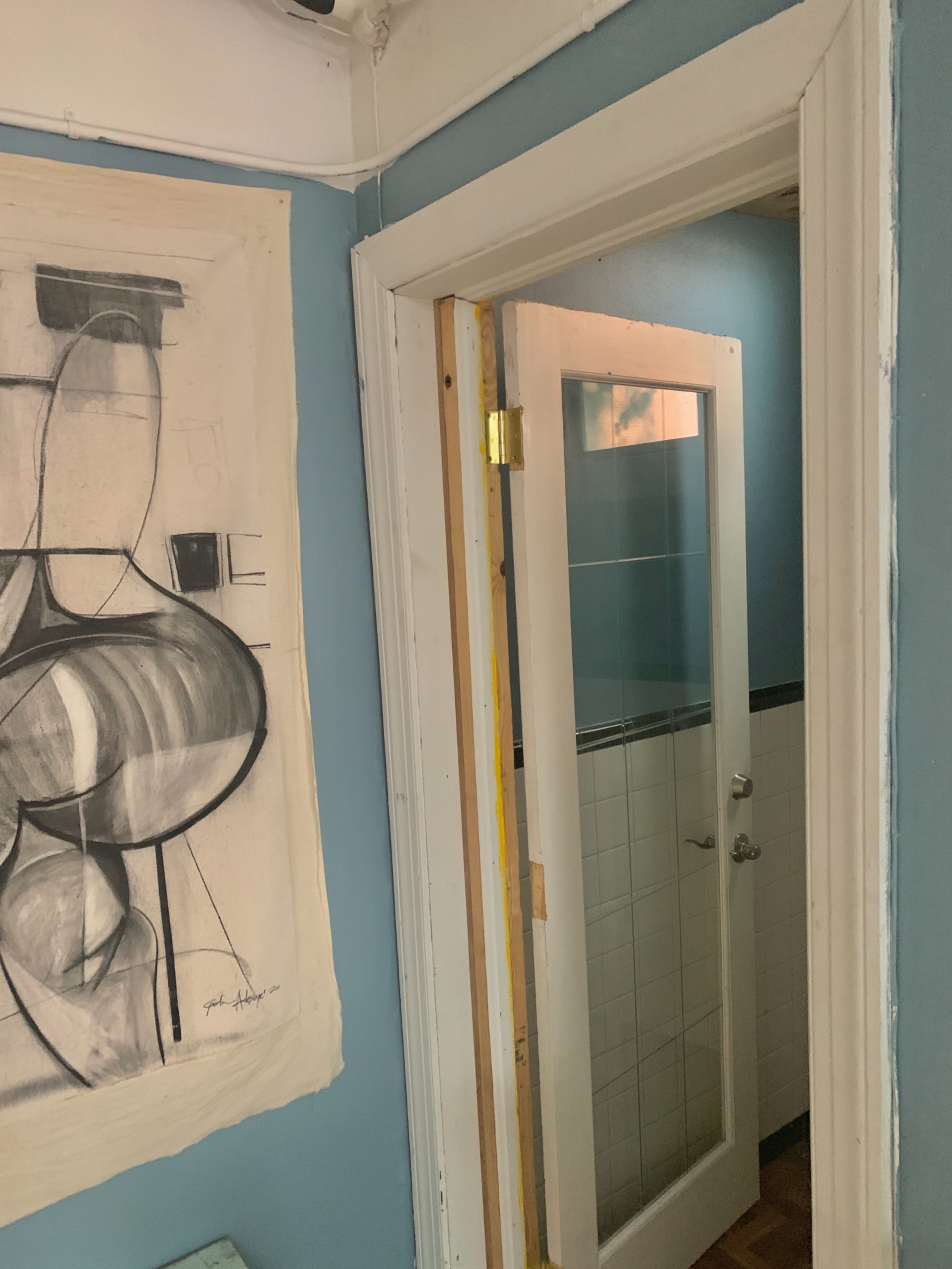 A doorway with a glass panel leads to a tiled bathroom, adjacent to a large abstract drawing on the wall.