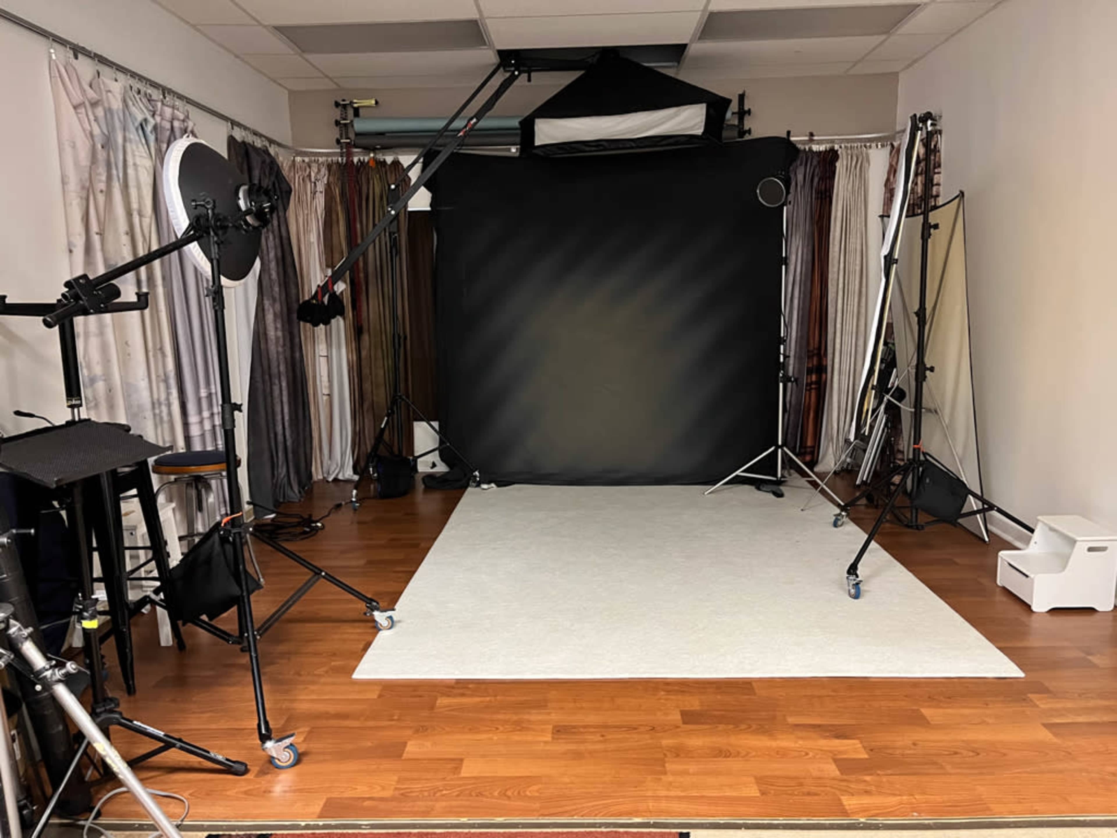 A photography studio with a black backdrop, lighting equipment, and a clean area for shooting on a light-colored floor.