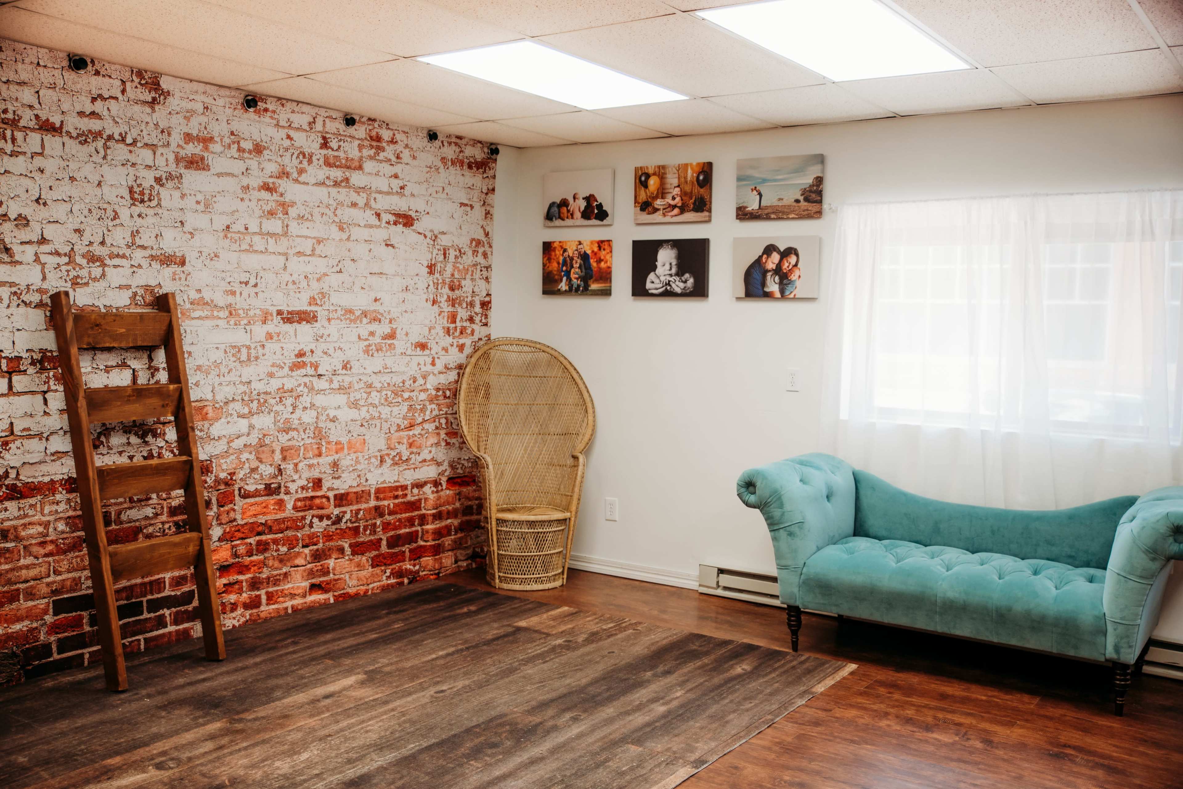 A room with a brick wall, a blue couch, a wooden ladder, and several framed photos on the white wall.