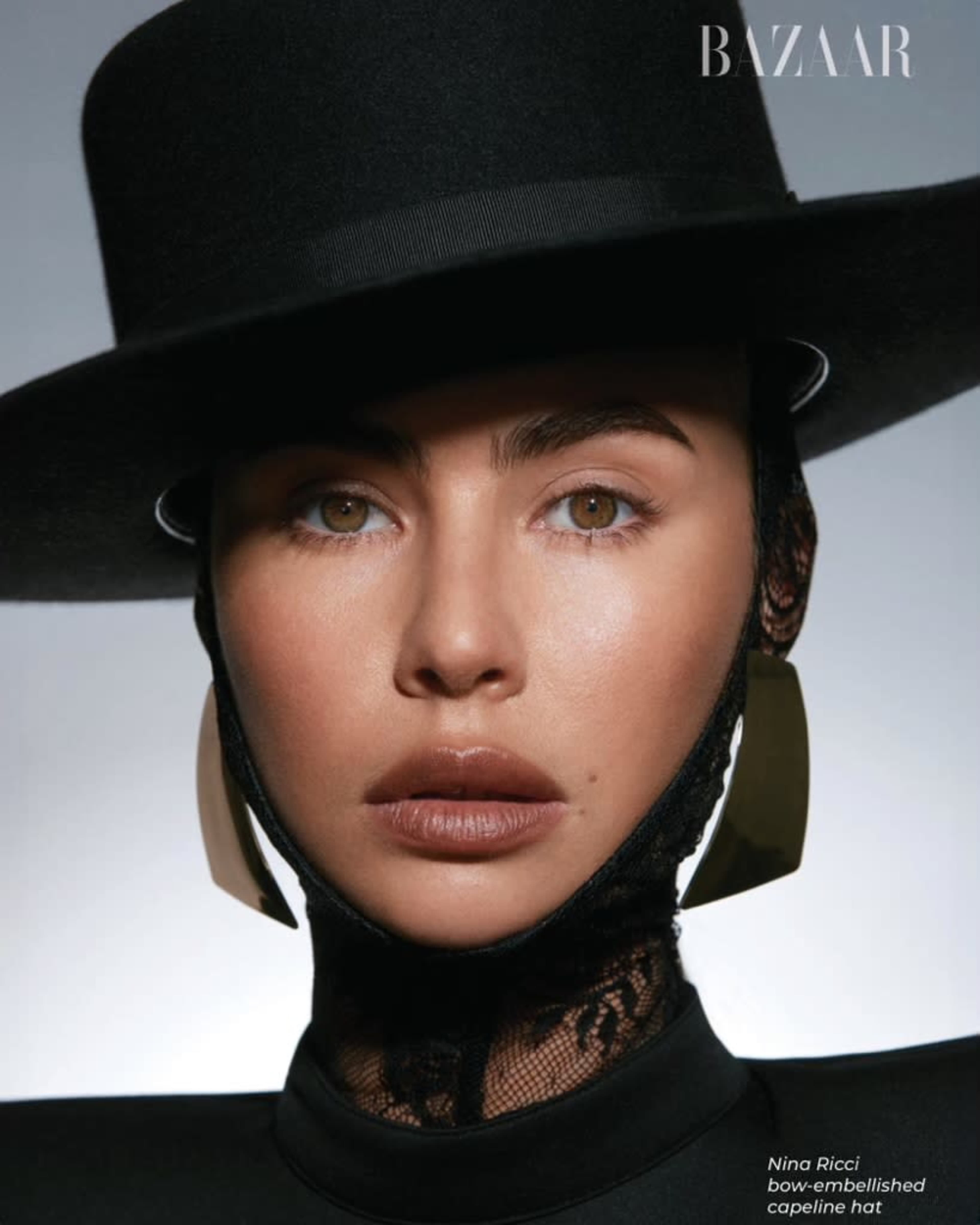 A woman wearing a large black hat and bold earrings, with her face partially framed by lace.