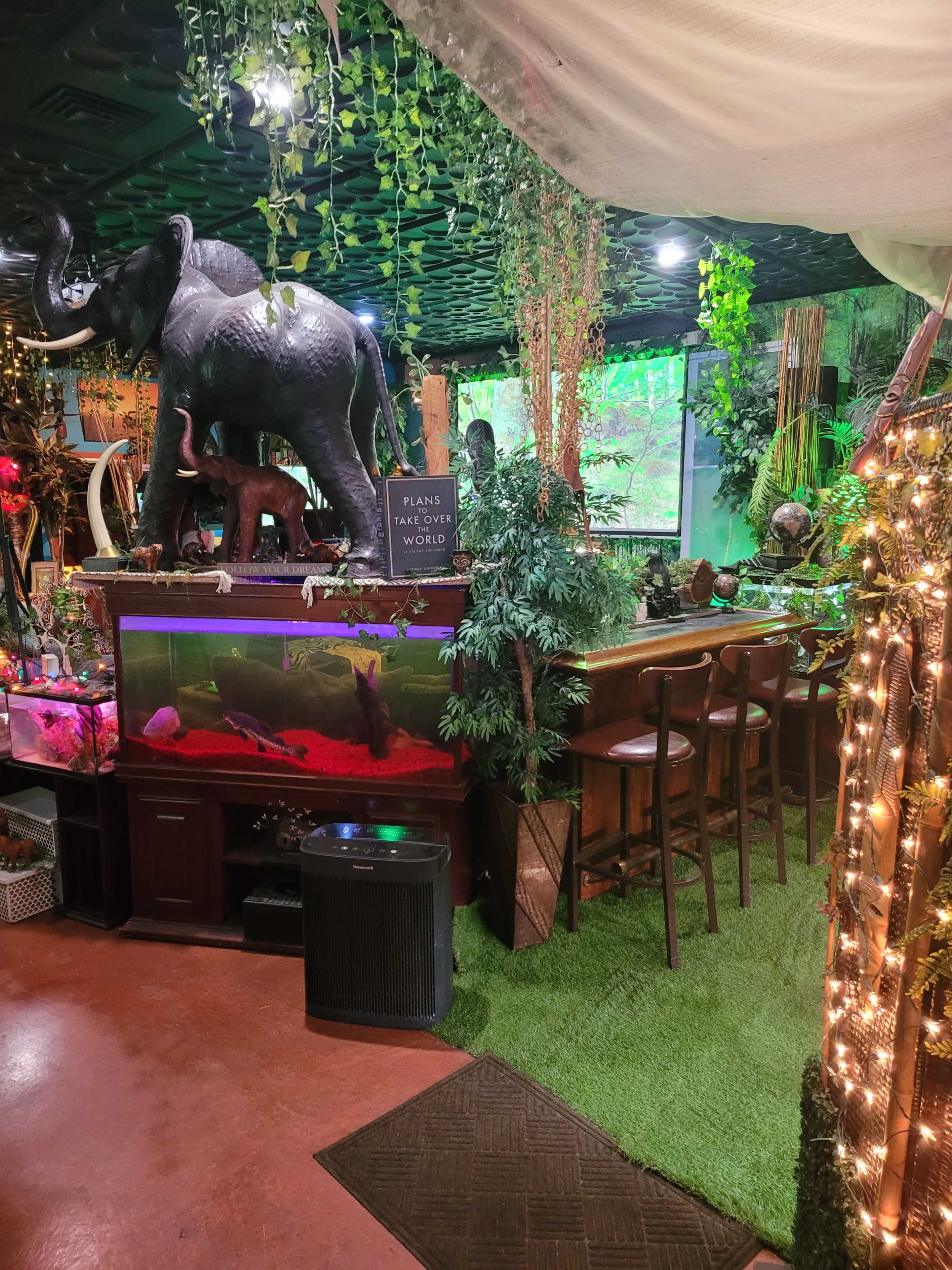 The scene features a themed bar area decorated with tropical plants, an elephant sculpture, and an aquarium, creating a jungle-like atmosphere.
