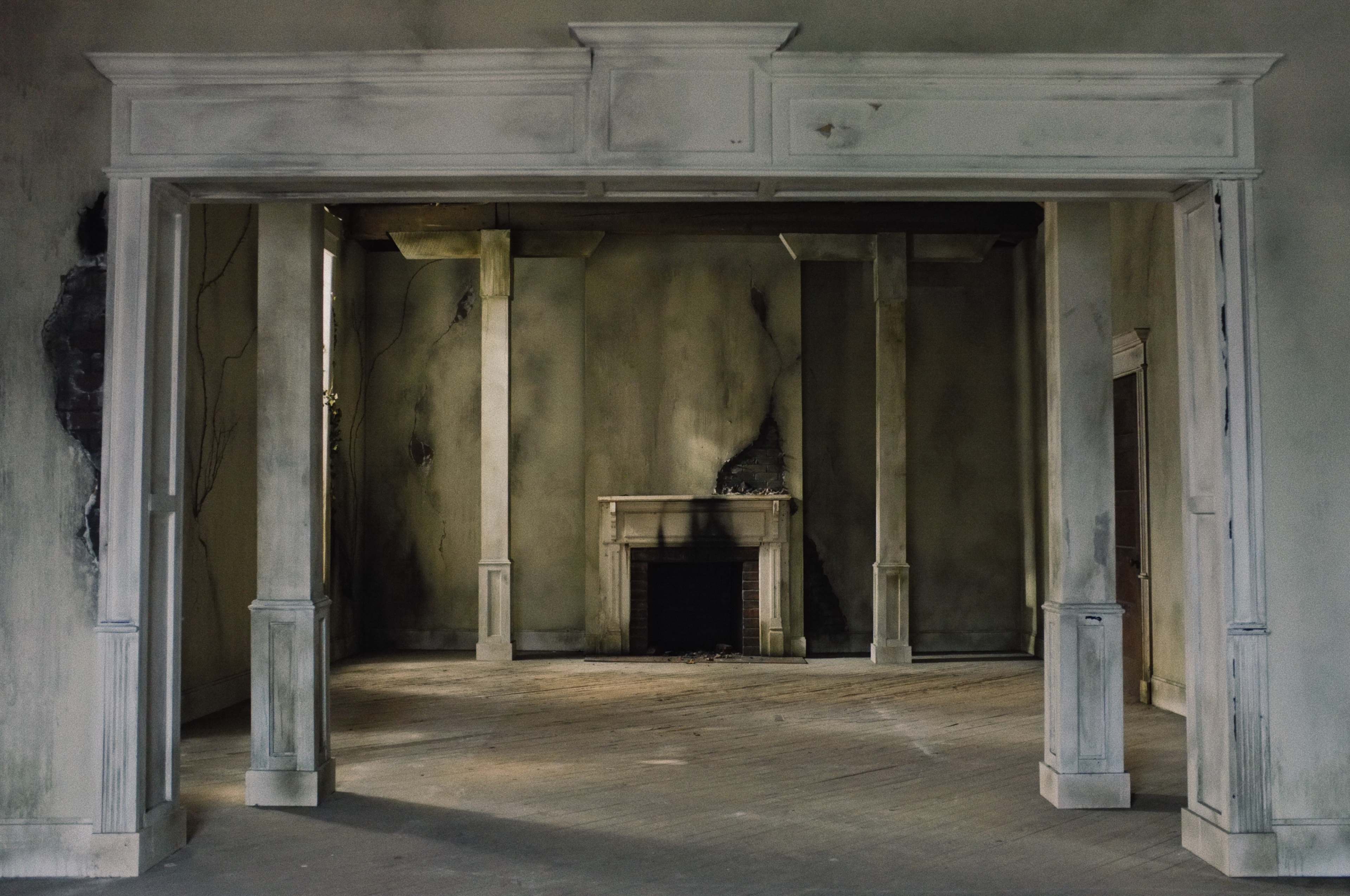 An empty and dilapidated room with a fireplace and white columns framing an entrance.