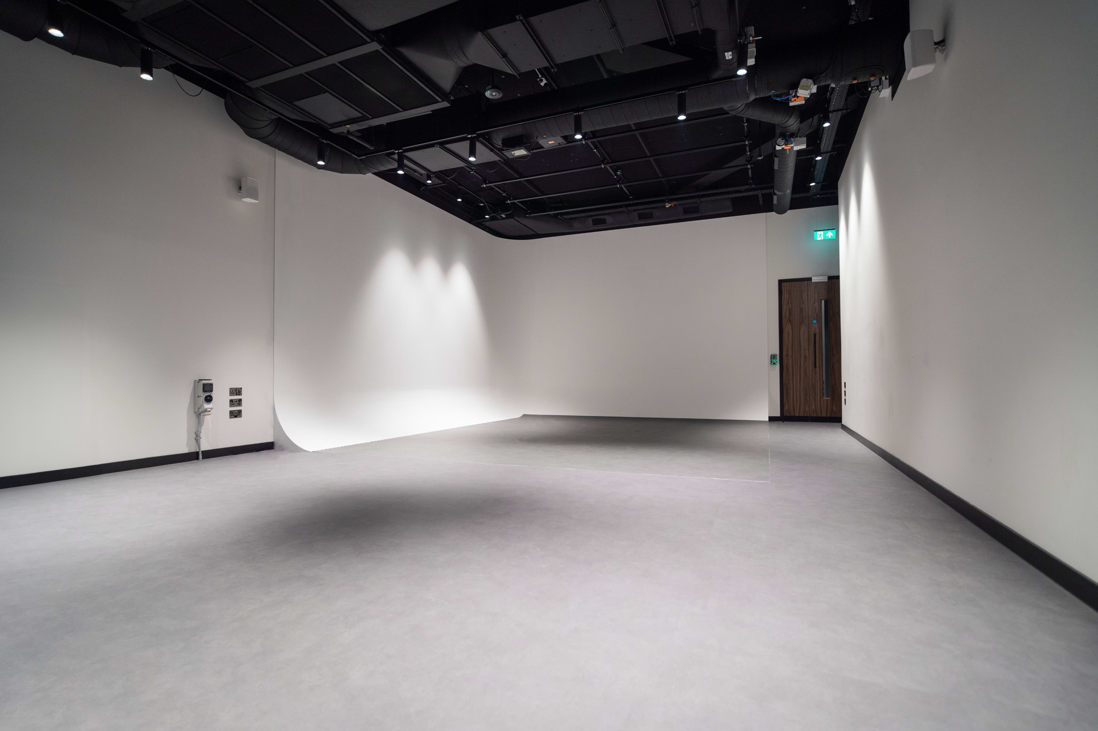 The image shows an empty studio space with white walls, a light gray floor, and a door on one side.