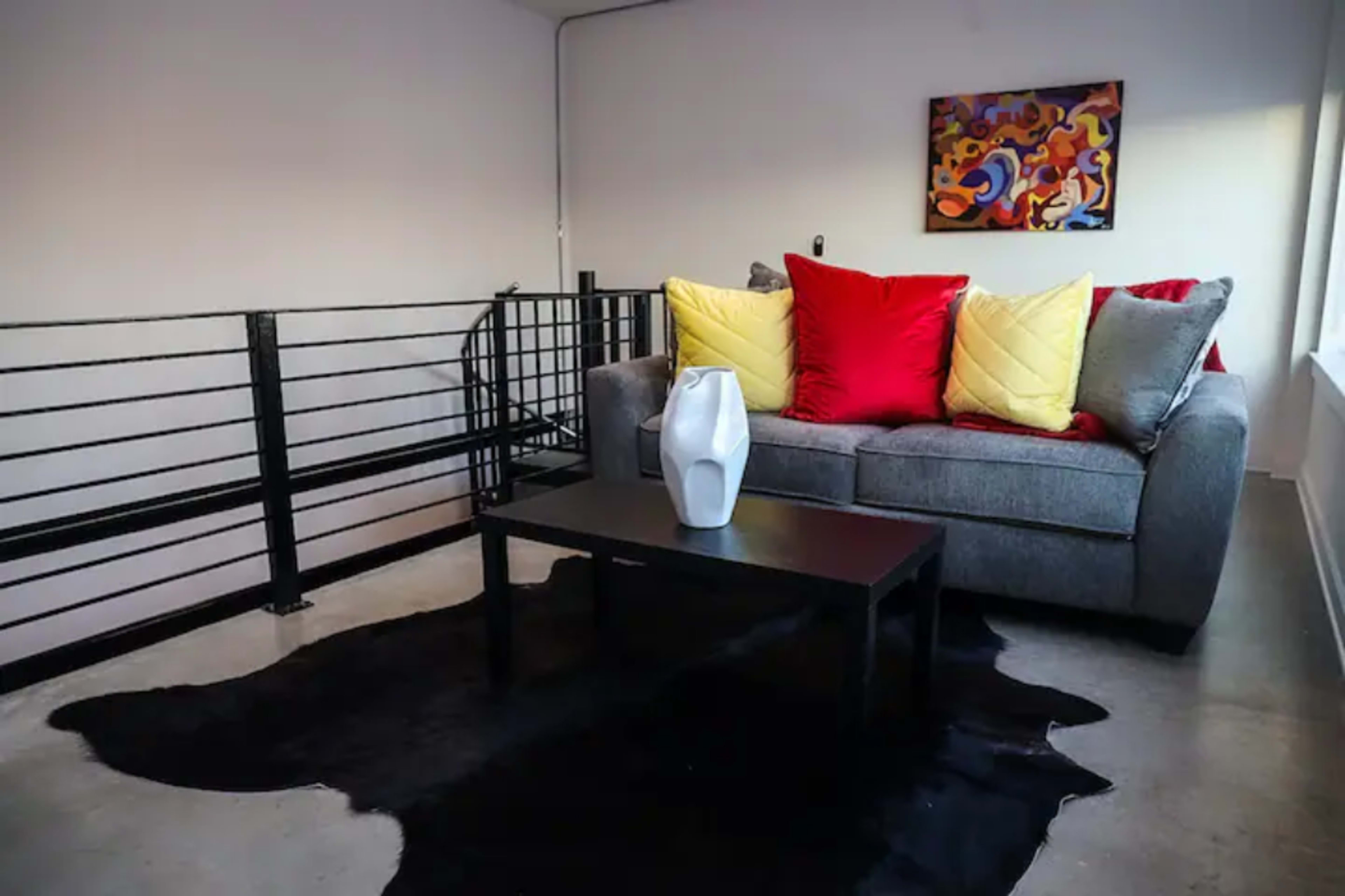A gray sofa with red and yellow pillows is positioned next to a black coffee table on a black cowhide rug in a modern living space.