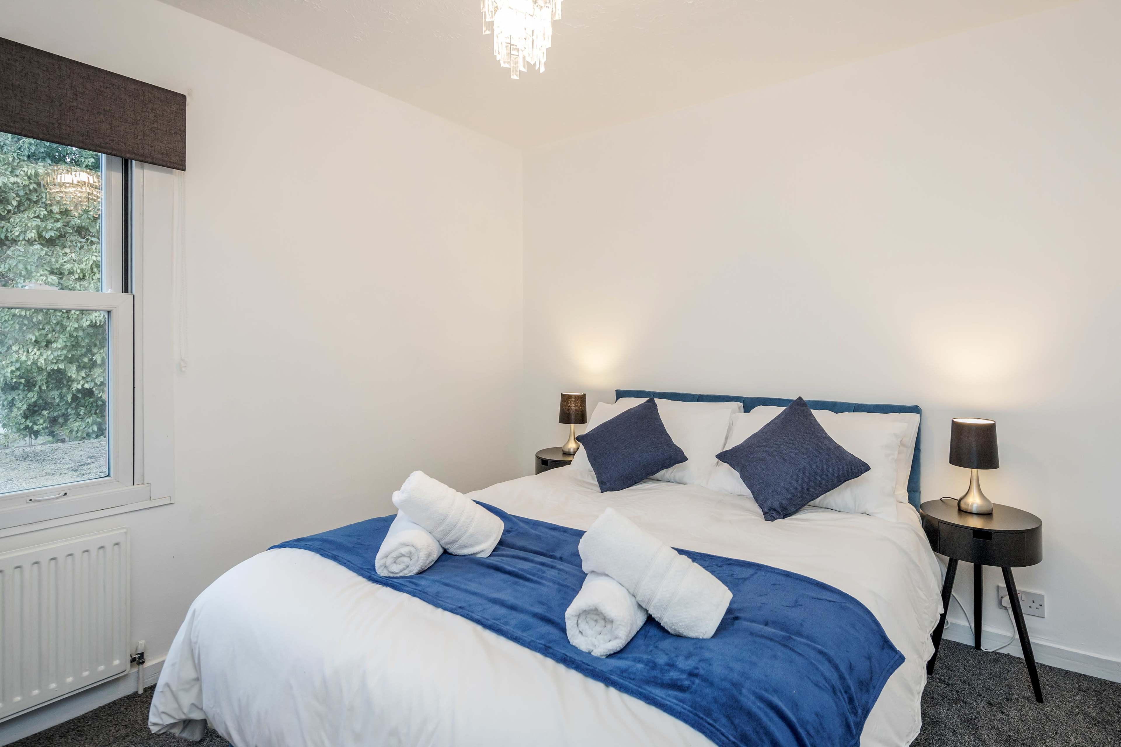 A bedroom with a large bed covered in white linens and a blue throw, flanked by two bedside tables with lamps.