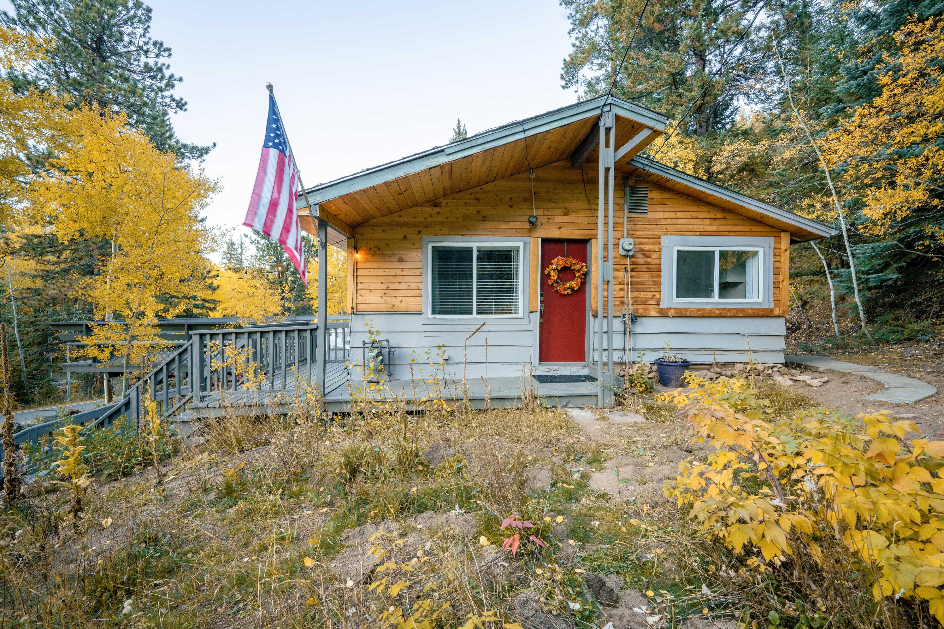 A wooden cabin with a red door and an American flag is set amidst autumn foliage.