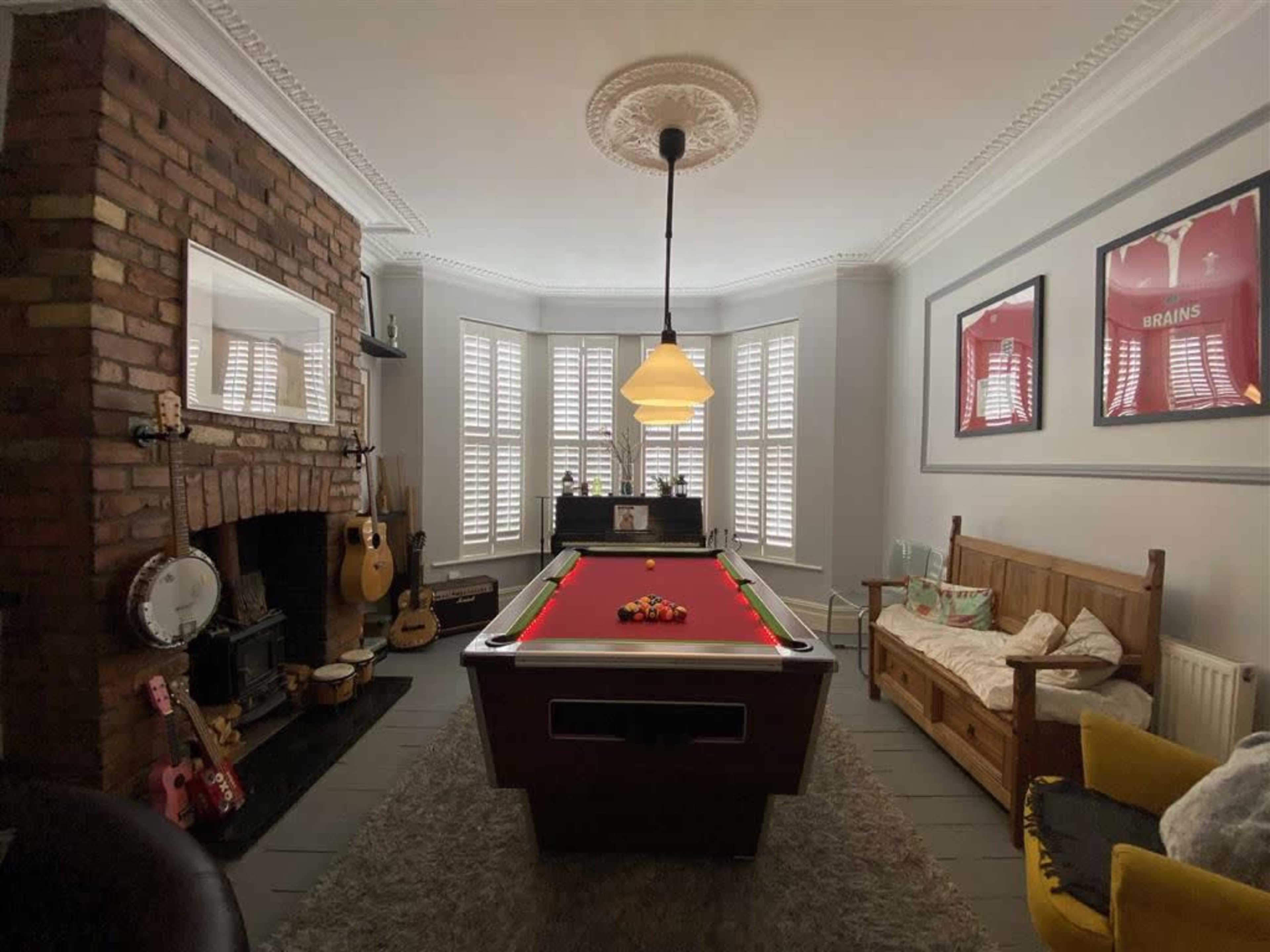 The room features a pool table at its center, surrounded by a brick fireplace, wooden furniture, and various musical instruments.