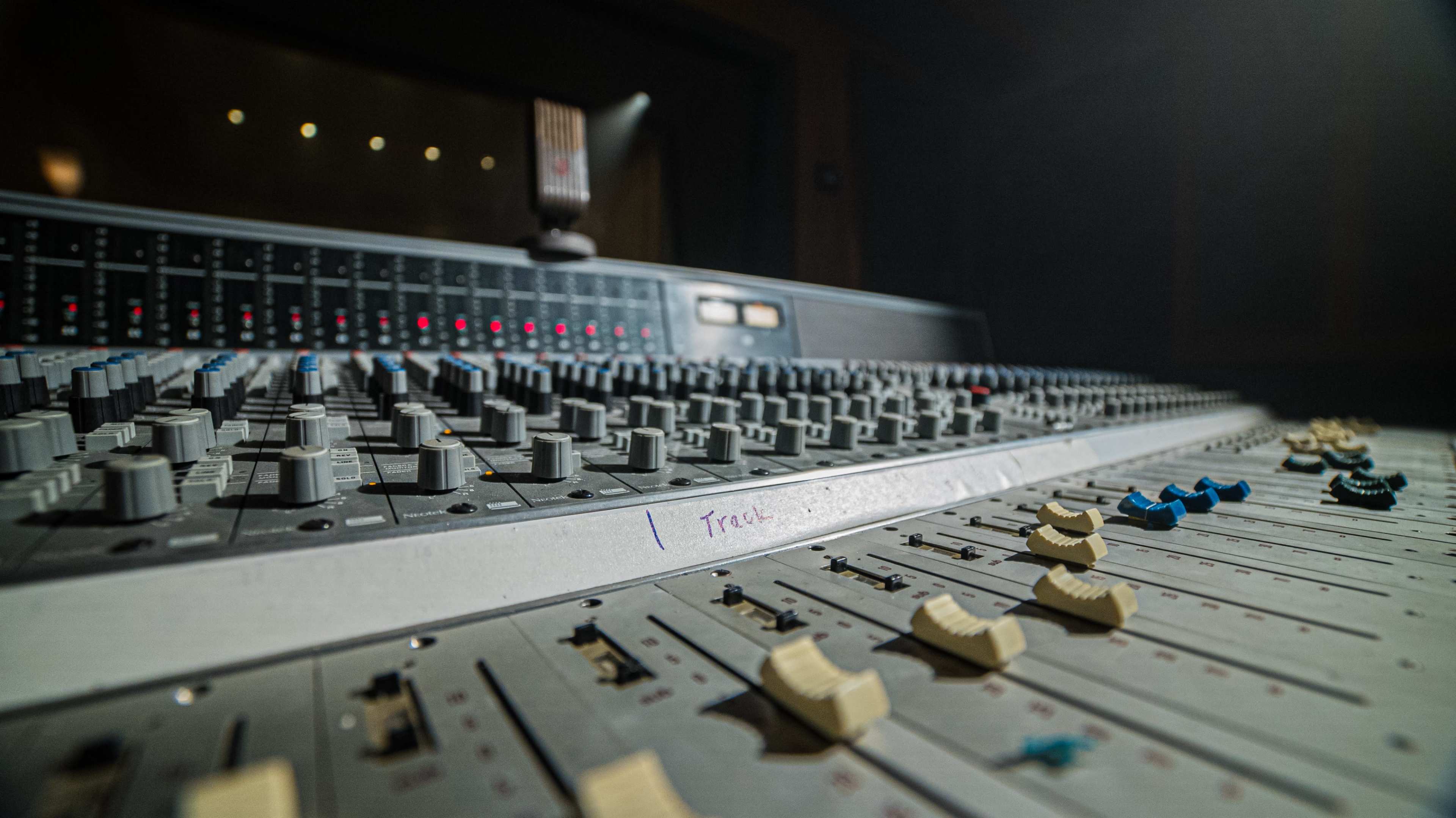 A close-up shot of a mixing console with various knobs and sliders, set in a dimly lit recording studio.