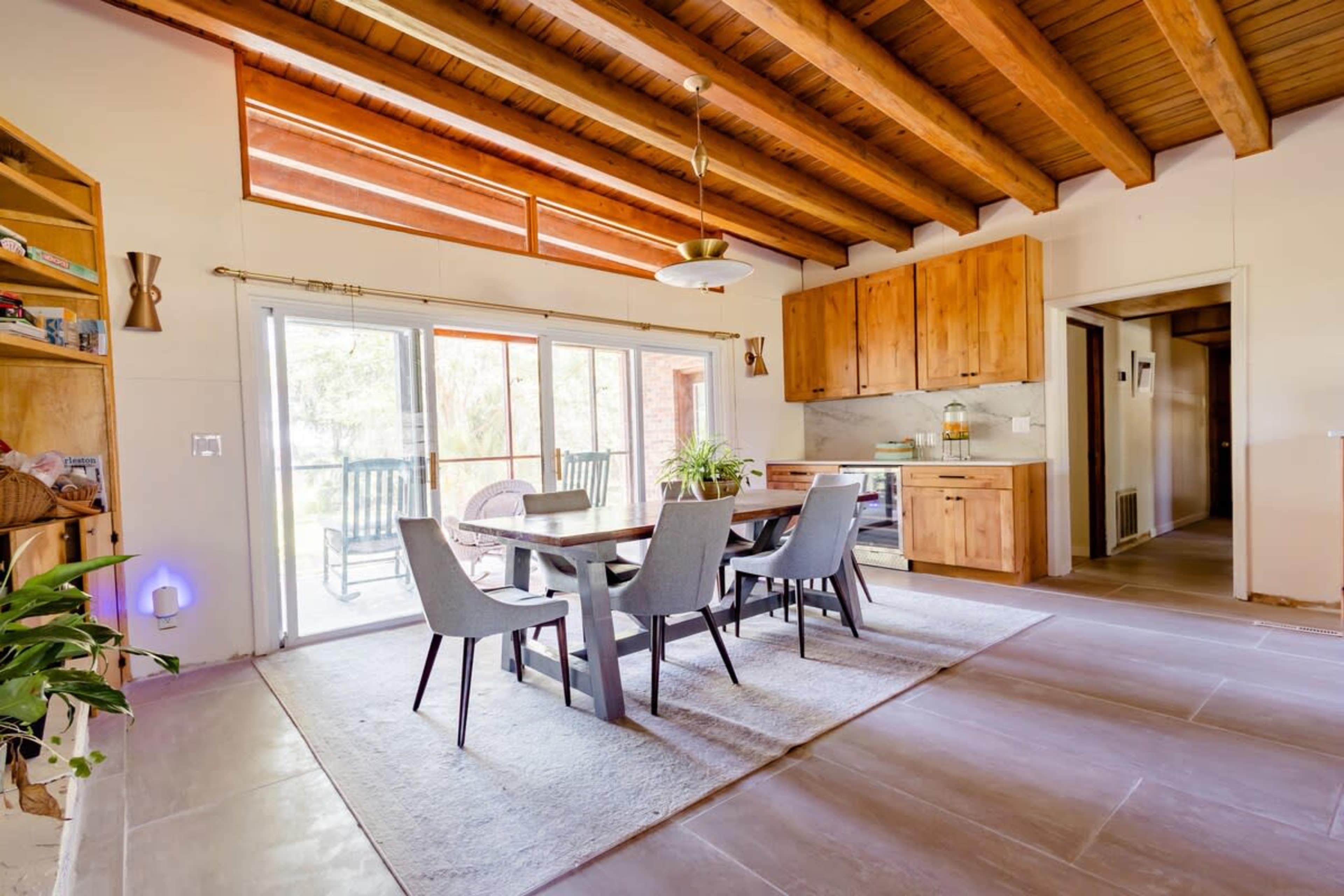 A modern dining area features a wooden table surrounded by gray chairs, with large windows allowing natural light to enter.