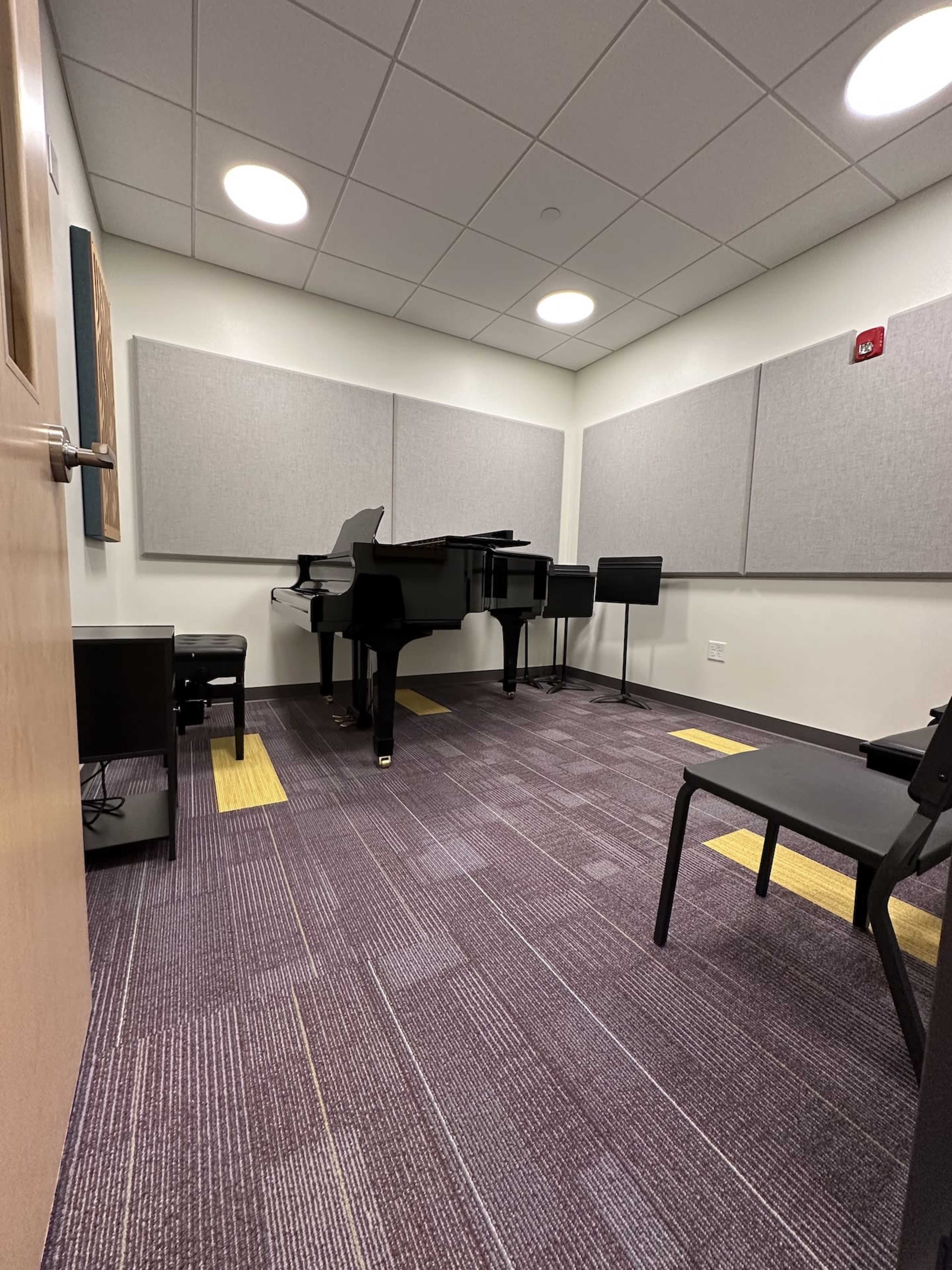A soundproof room with a black grand piano, two chairs, and acoustic panels on the walls.