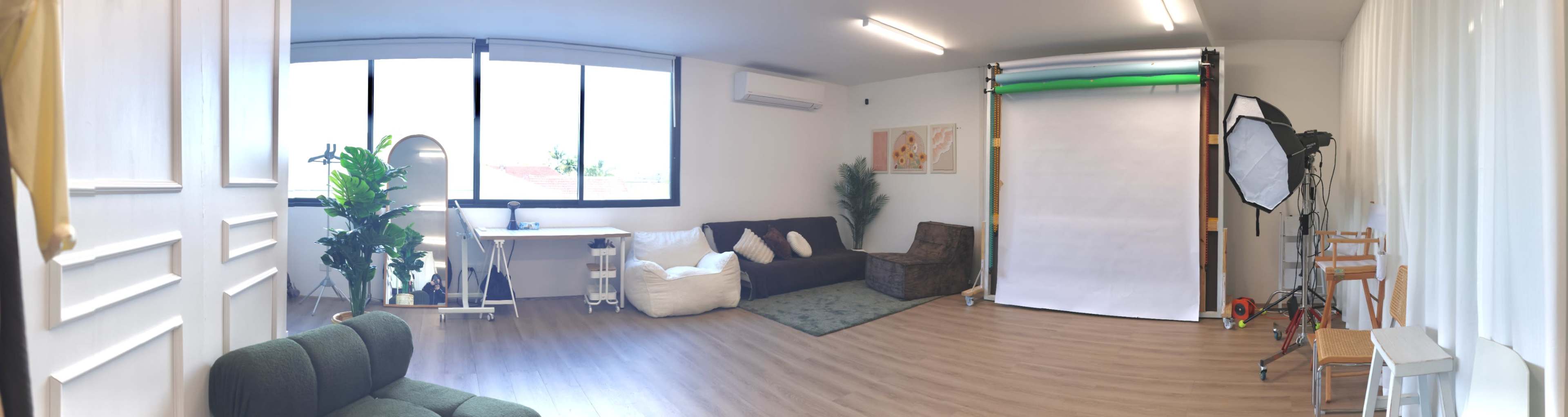 The image shows a bright, modern studio space with a seating area, a table, and a backdrop setup for photography.