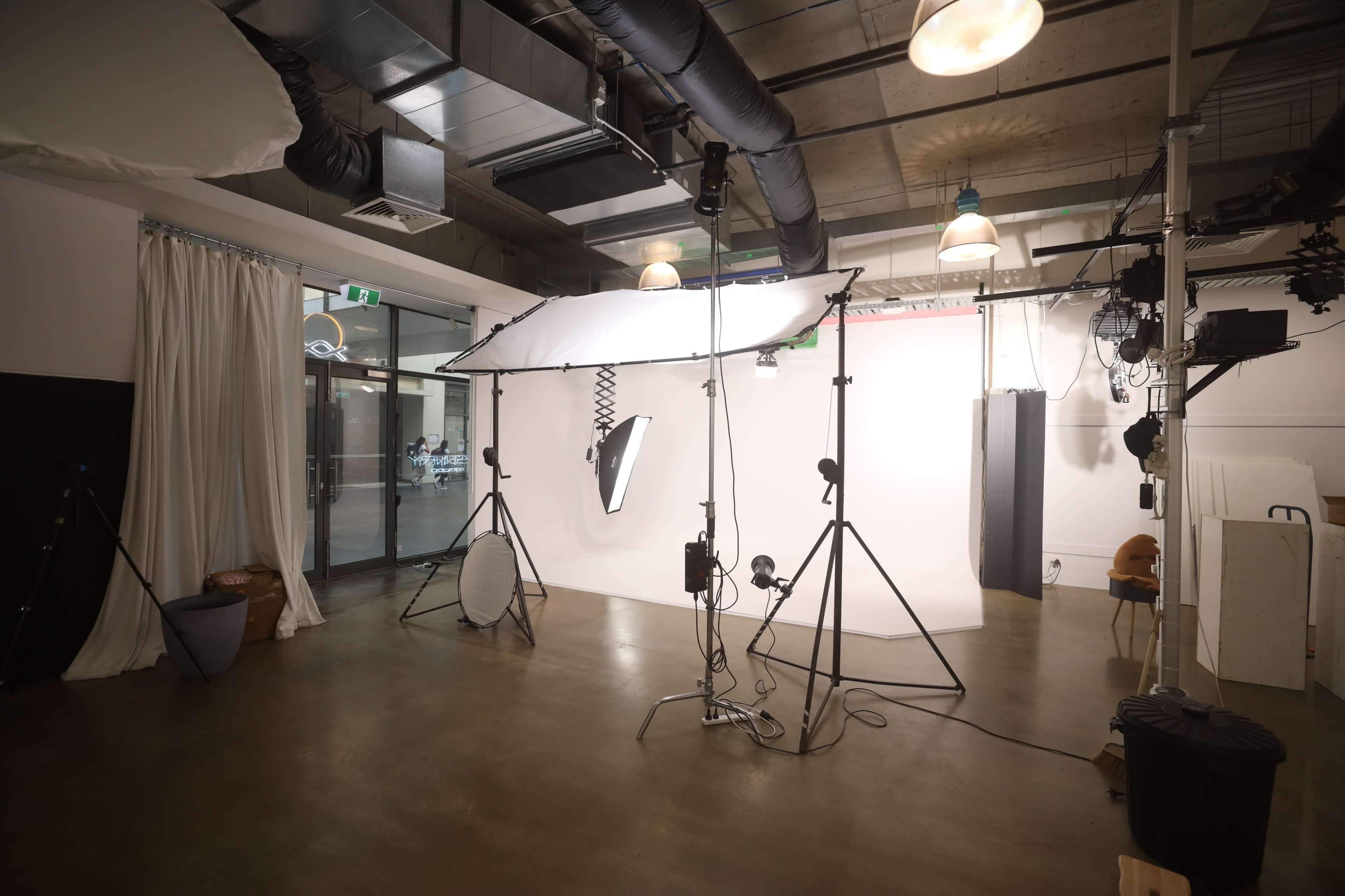 The image shows a photography studio with various lighting equipment set up in front of a backdrop.