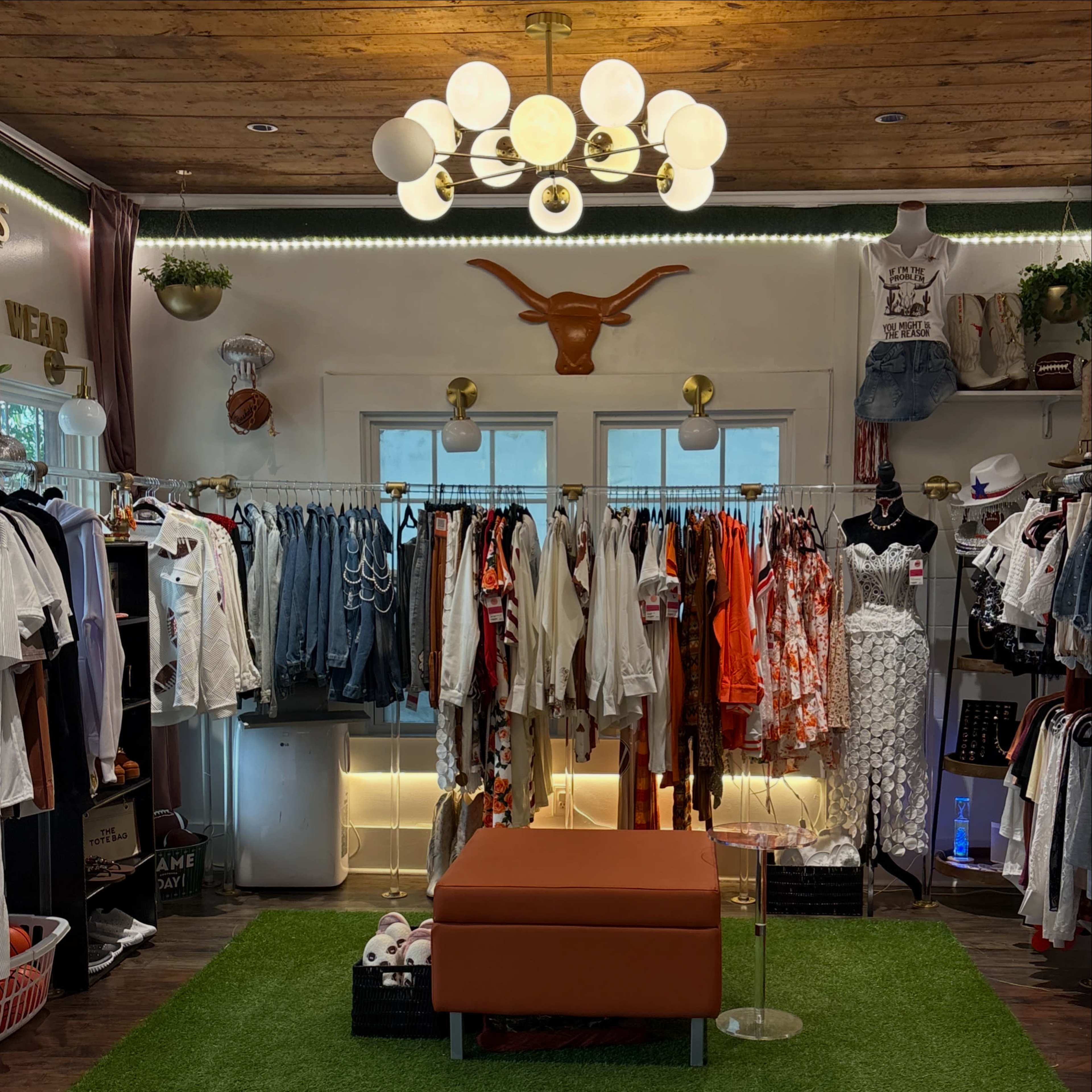 The image shows an interior of a boutique featuring a variety of clothing racks, a central orange seating area, and decorative lighting.