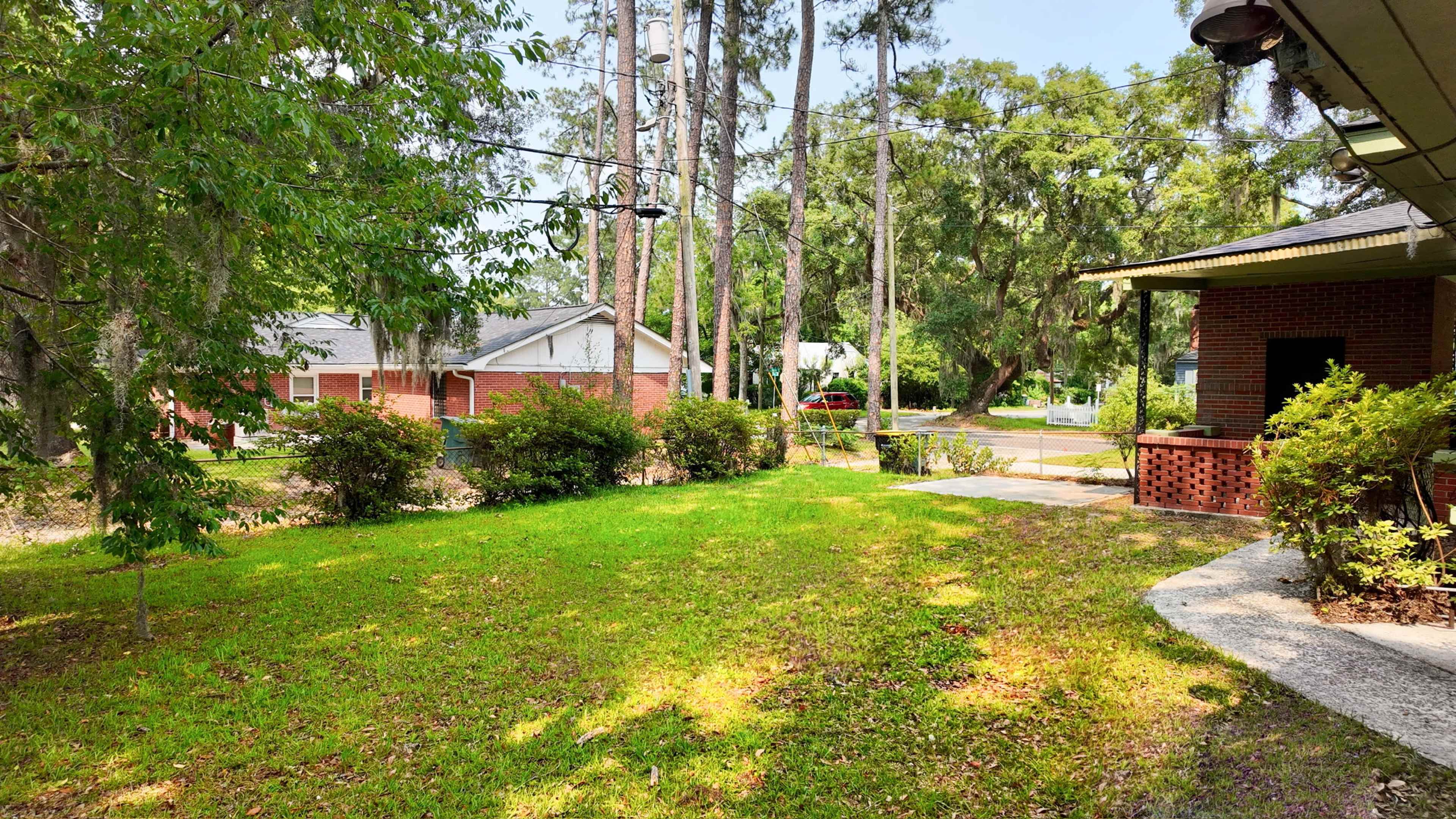 The image shows a grassy yard with a pathway, surrounded by trees and shrubs, and houses visible in the background.
