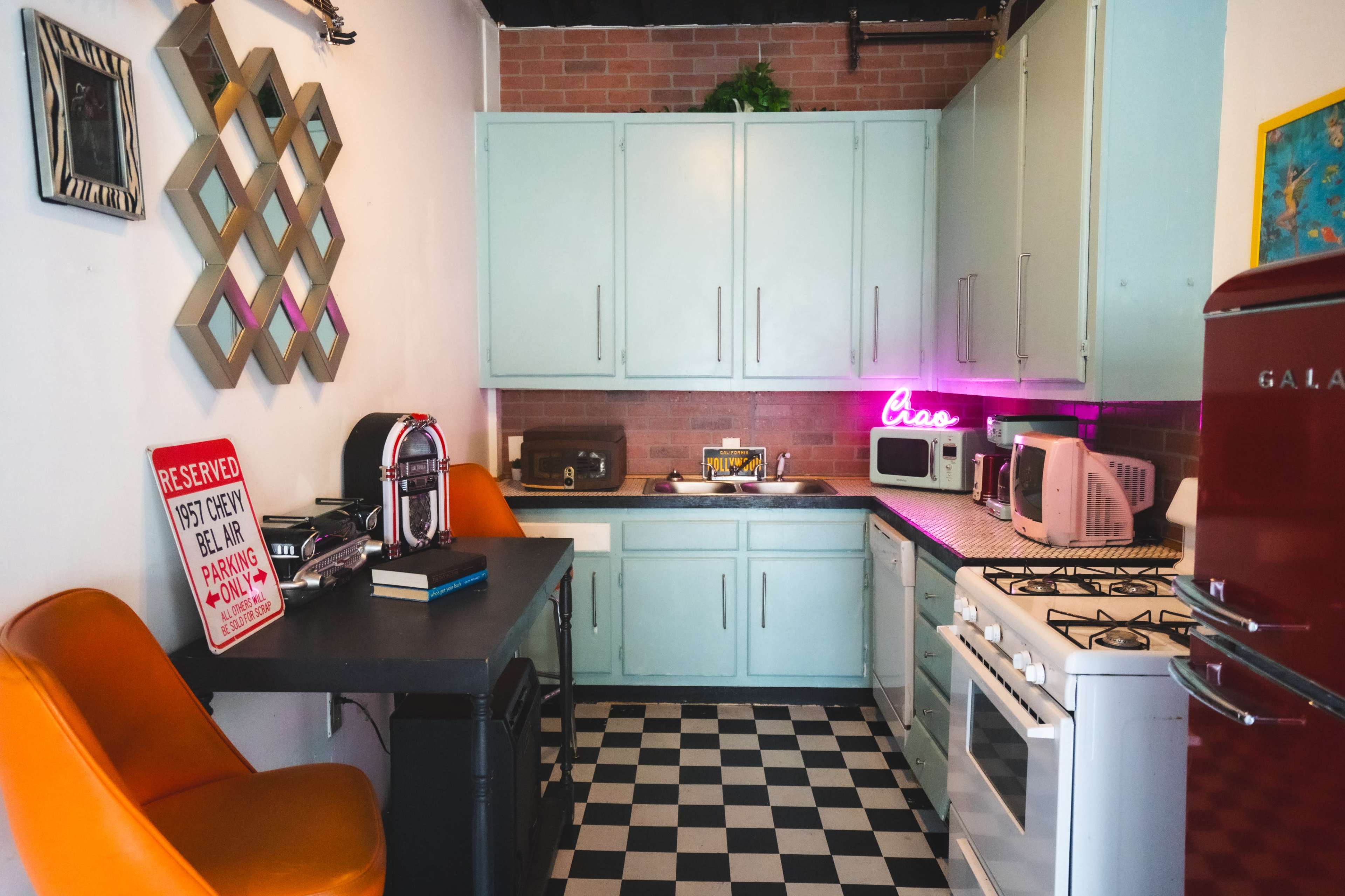 A compact kitchen features mint green cabinets, a black and white checkered floor, and retro appliances, including a red refrigerator and a coffee maker.