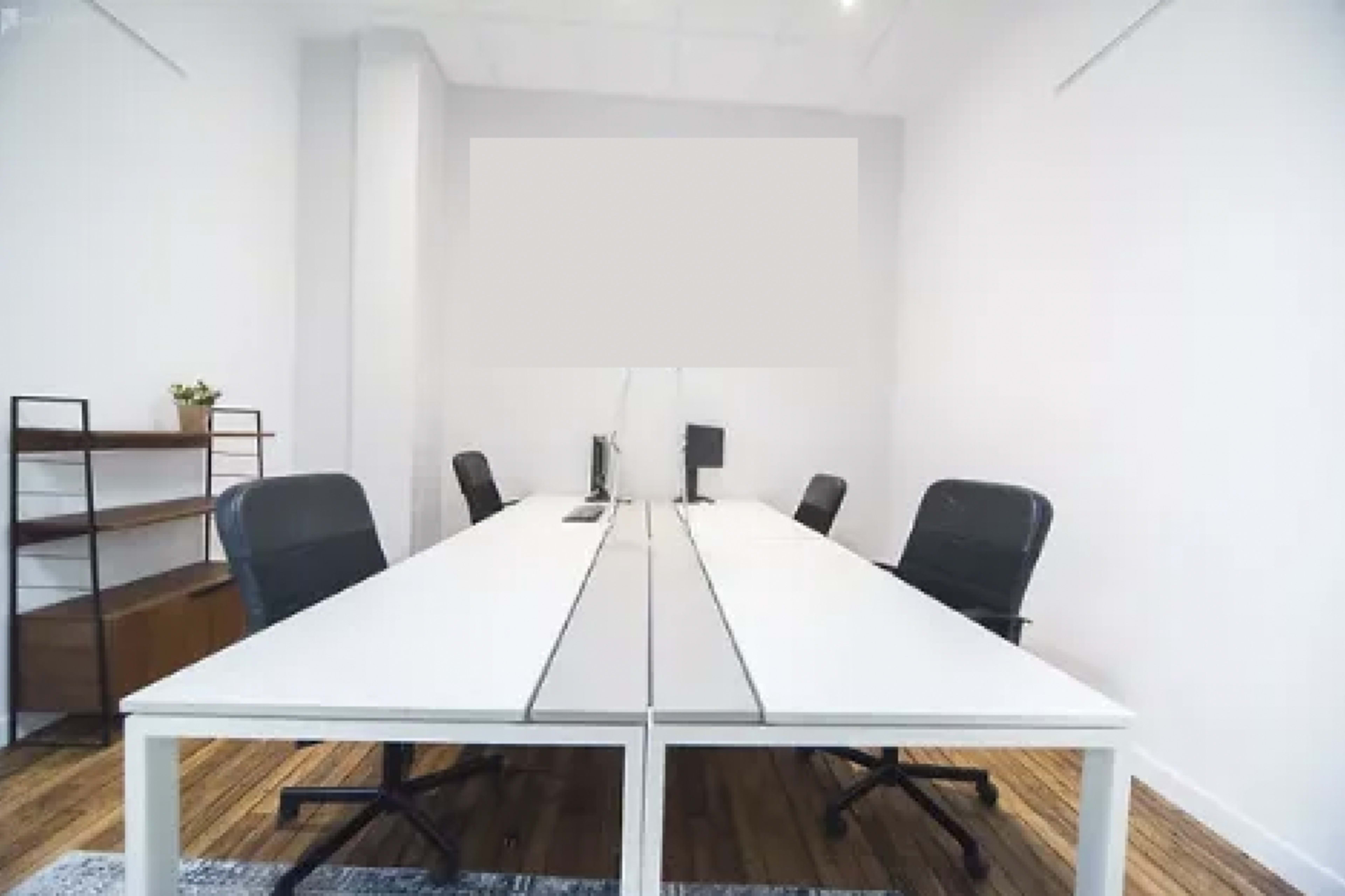A minimalistic office space with a long white table, black chairs, and a bookshelf.