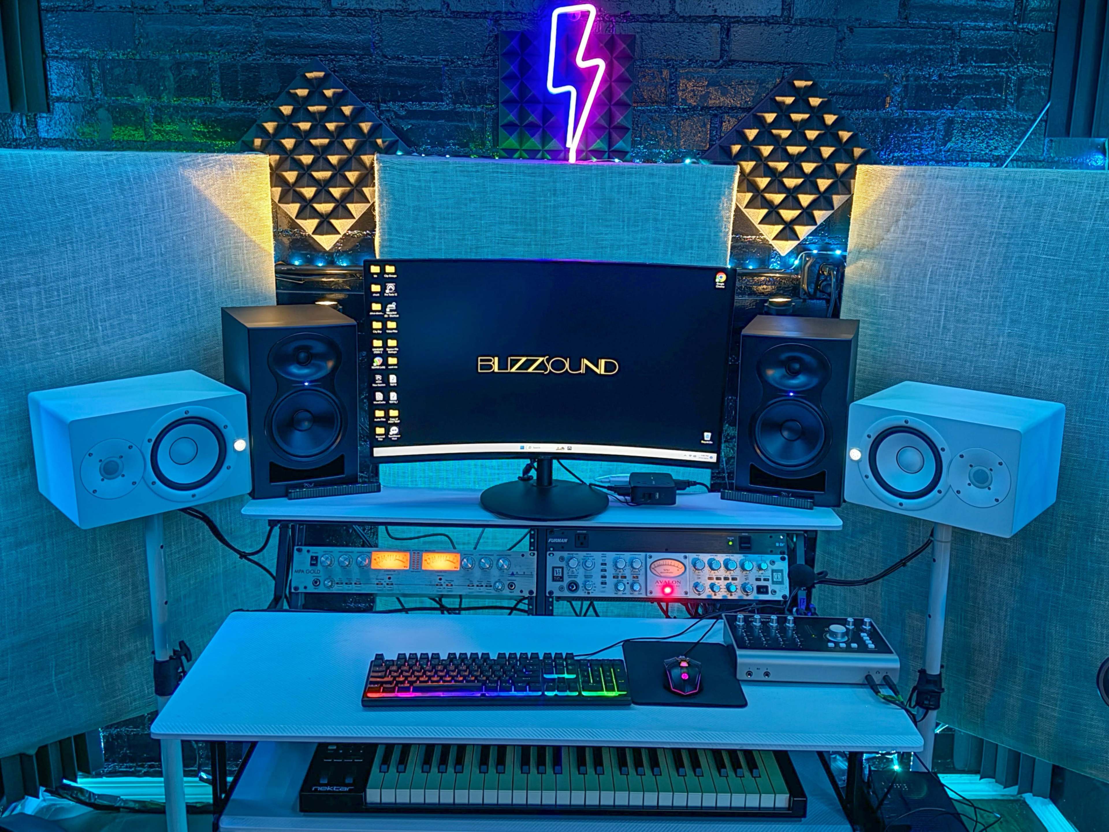 A music production setup with a curved monitor, two pairs of studio monitors, a MIDI keyboard, and various audio equipment against a backdrop of illuminated soundproofing panels.