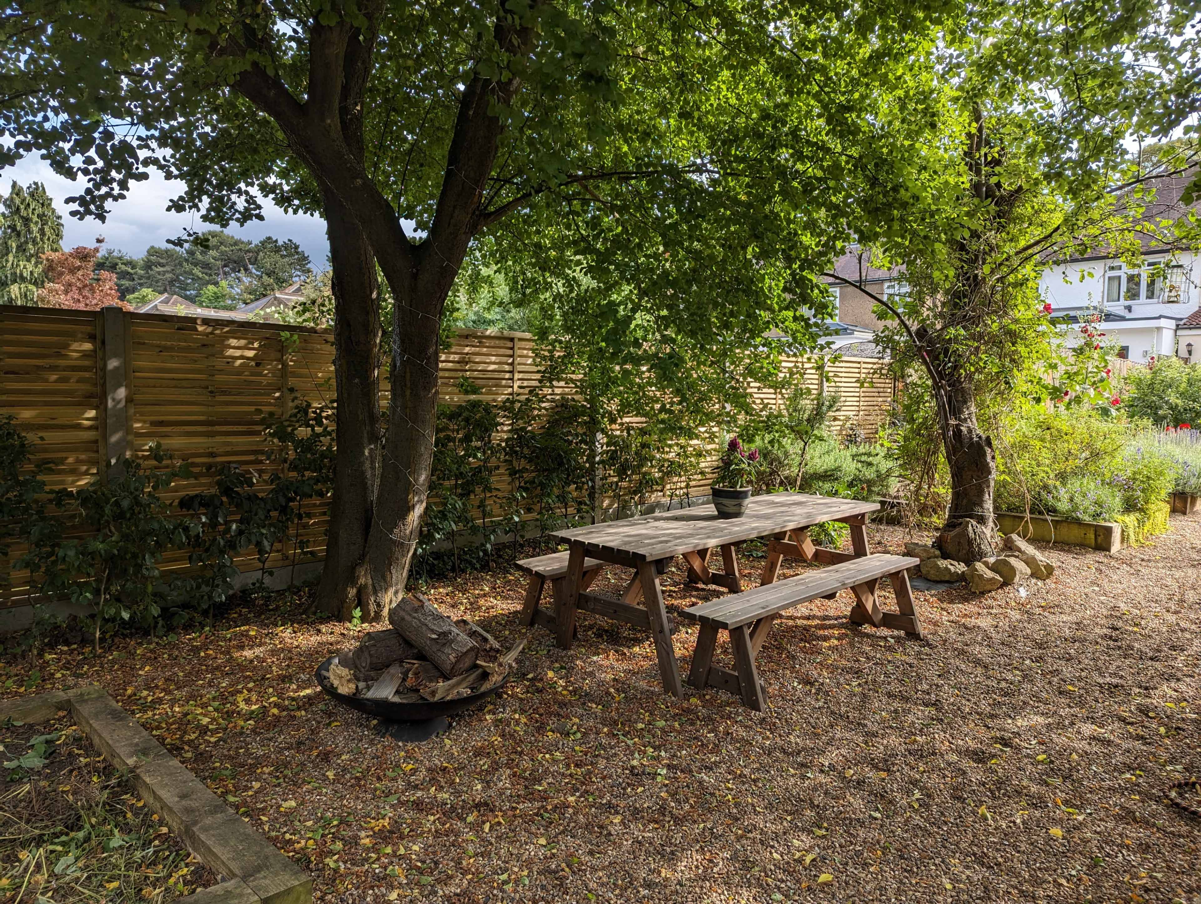 A wooden picnic table is surrounded by trees and gravel in a quiet garden.