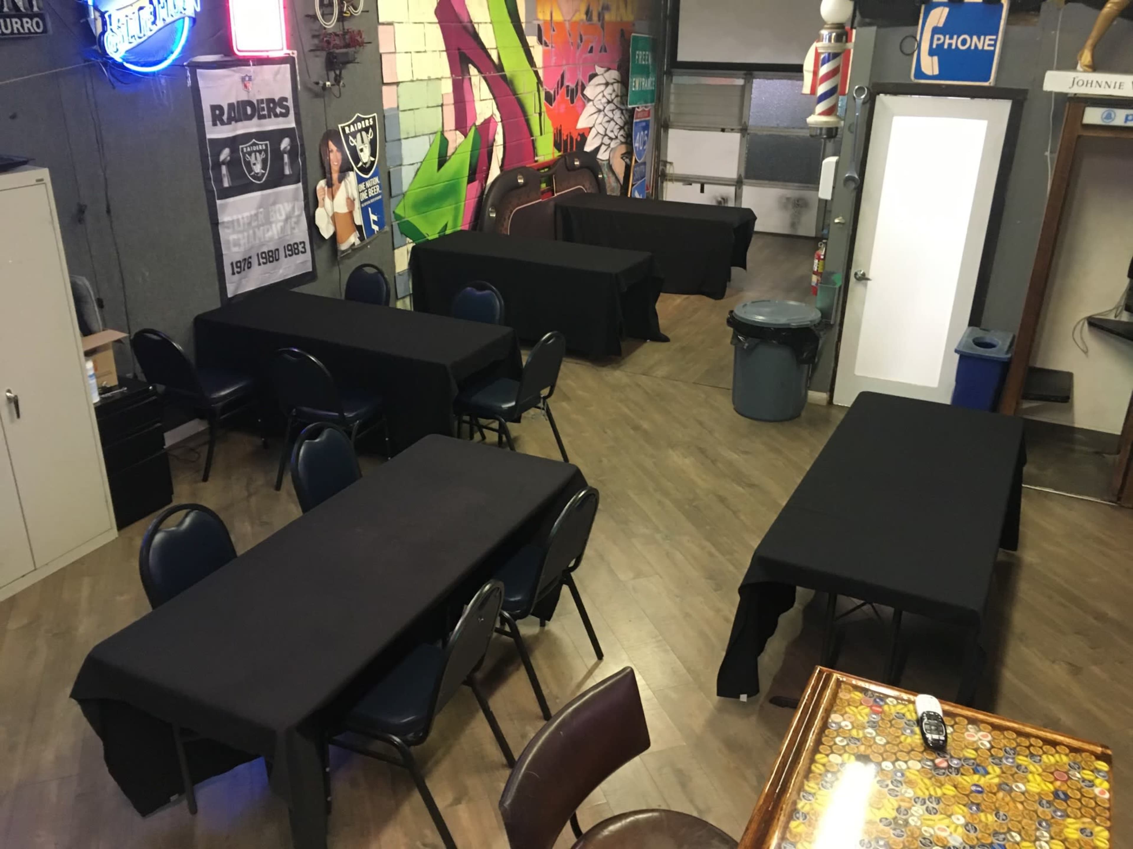 A room with several tables covered in black cloth, surrounded by chairs, and decorated with a mural and colorful signage.