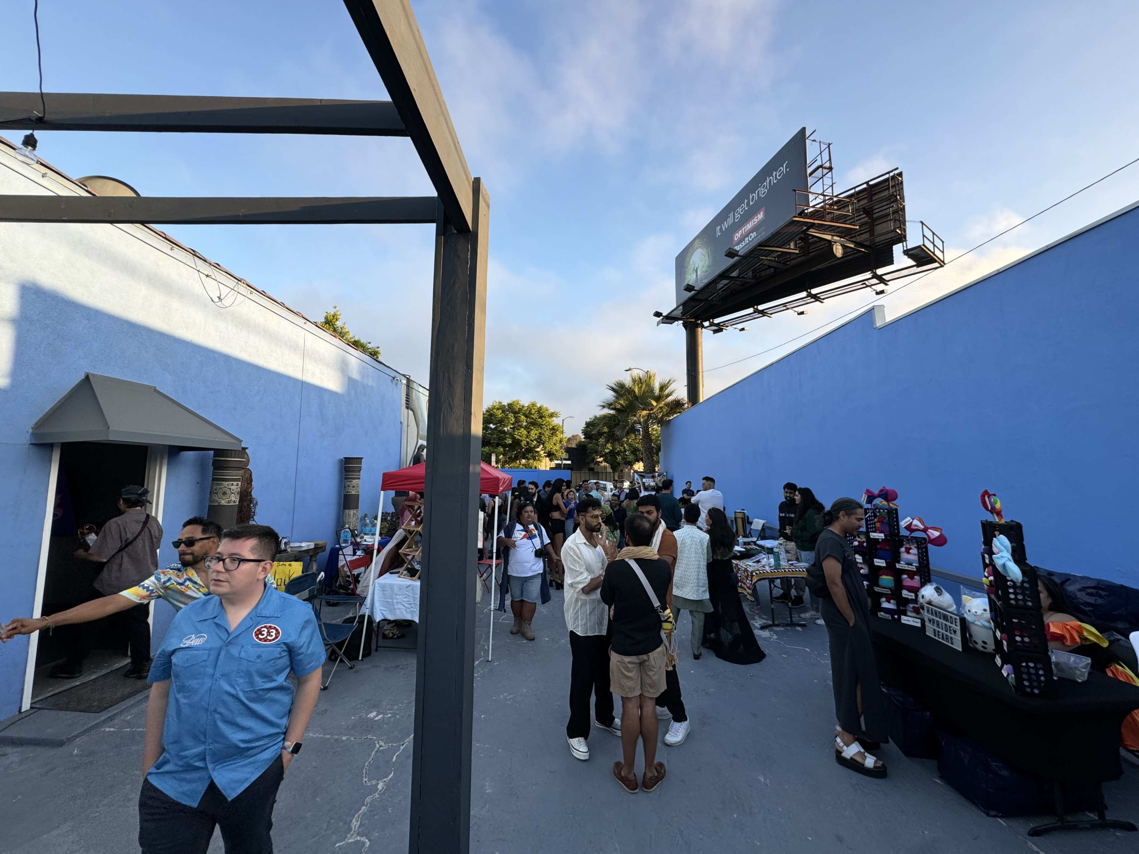 A crowd gathers in an outdoor space featuring vendor booths and a large billboard in the background.