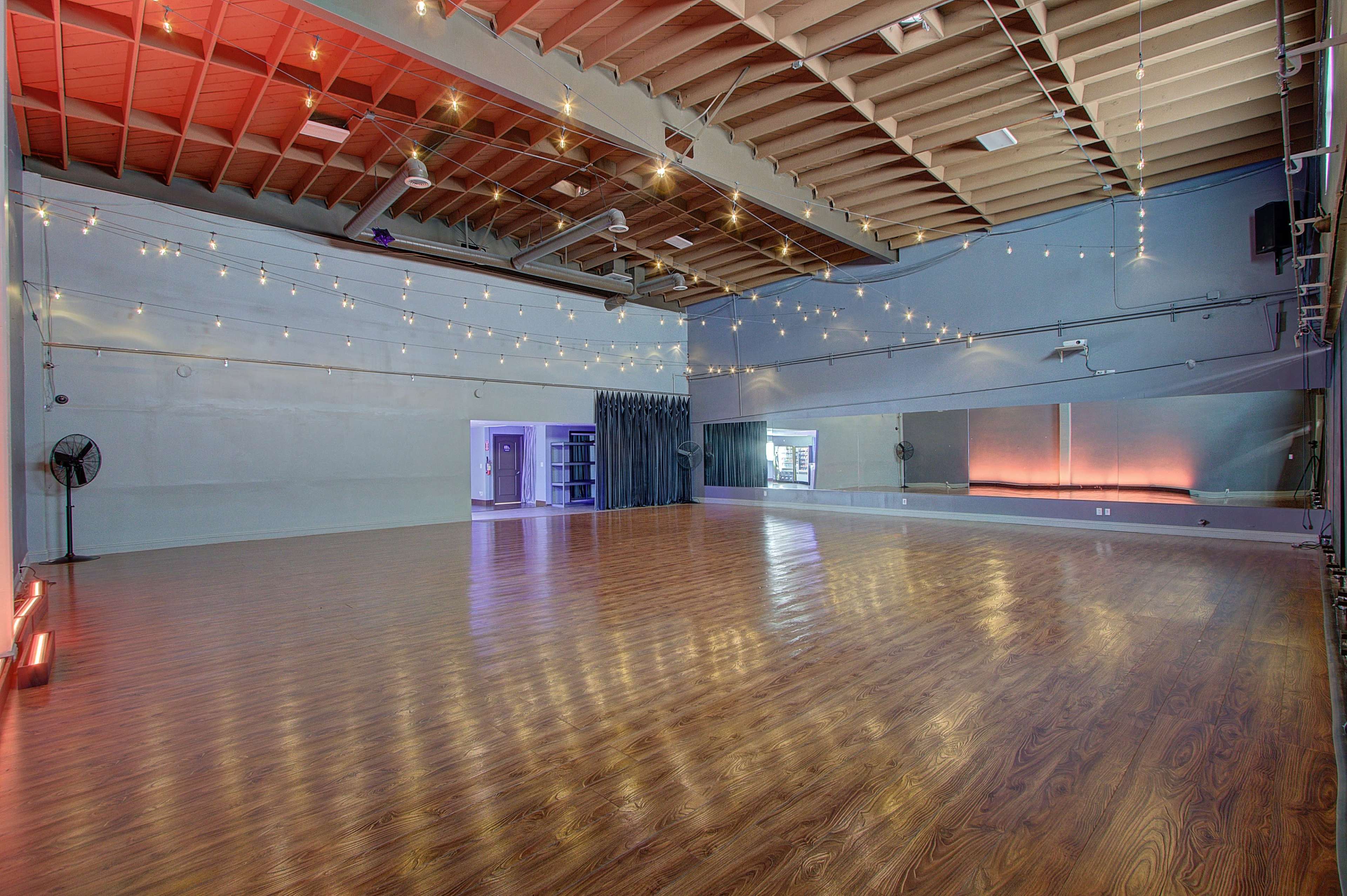 A spacious dance studio features polished hardwood floors, mirrored walls, and decorative ceiling lights.