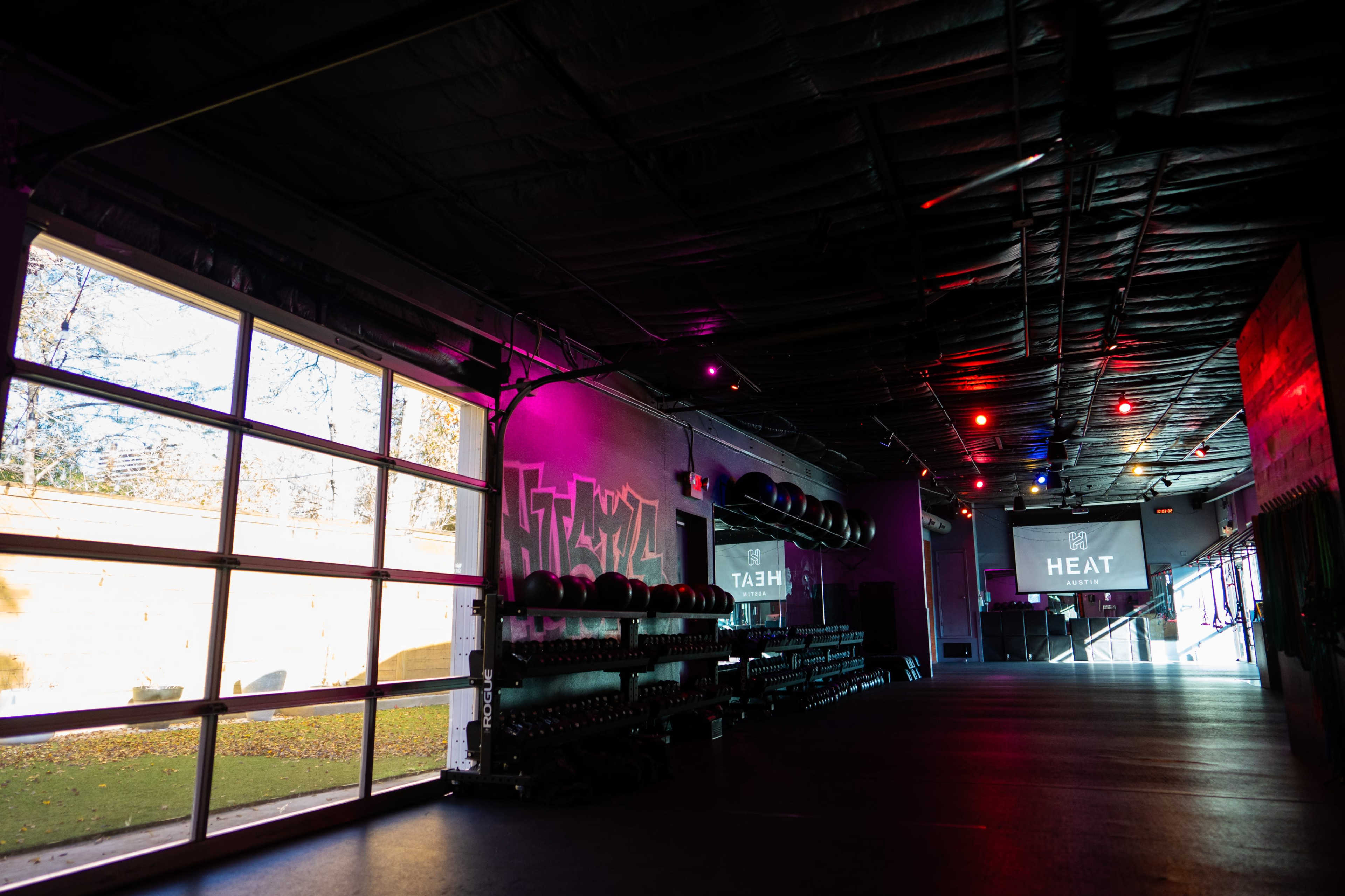 A fitness studio with exercise equipment lined up against the wall, illuminated by colored lights and featuring a projector screen displaying the word "HEAT."