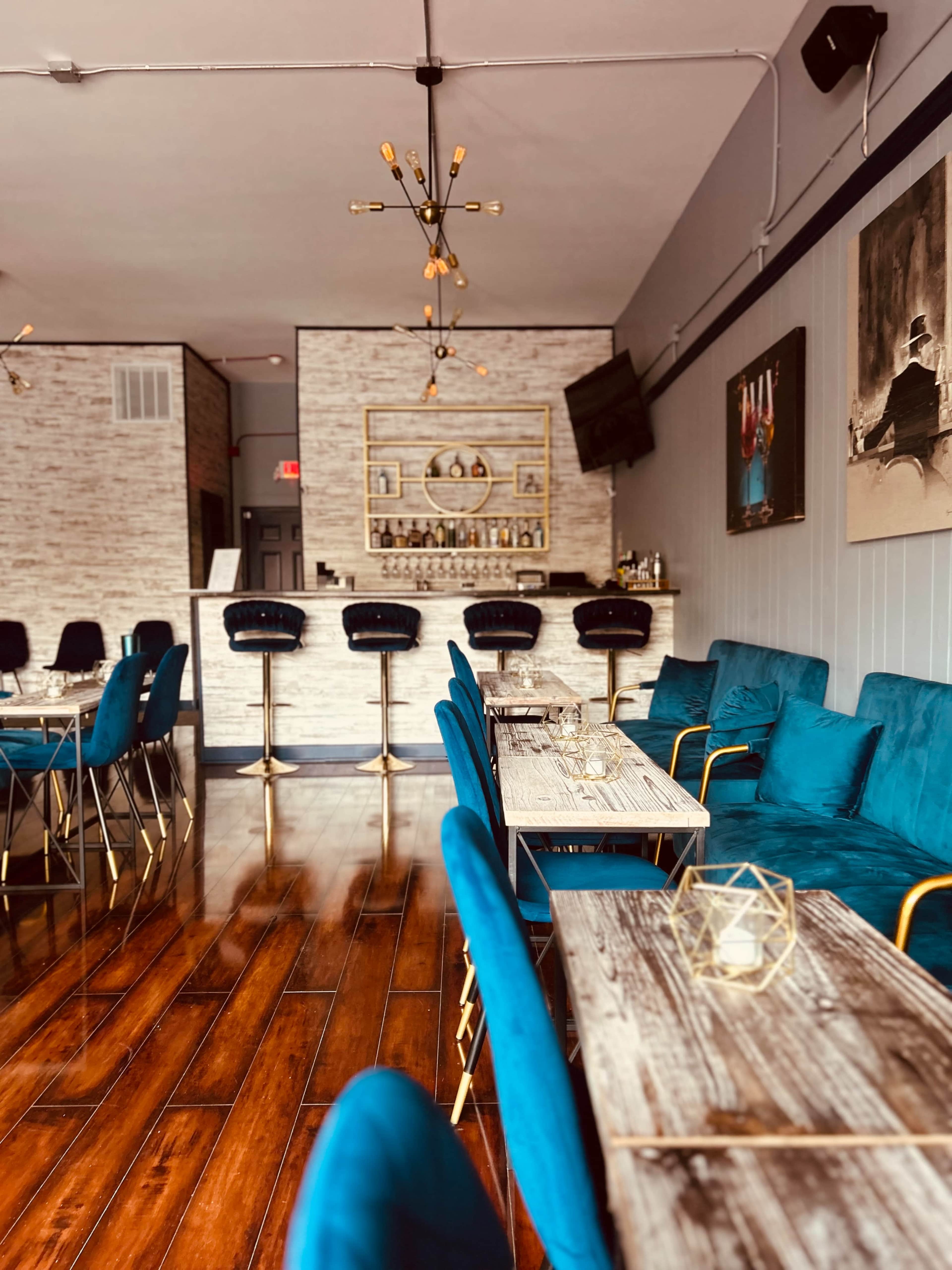 The image shows a contemporary restaurant interior with blue upholstered seating, wooden tables, and a bar area in the background.