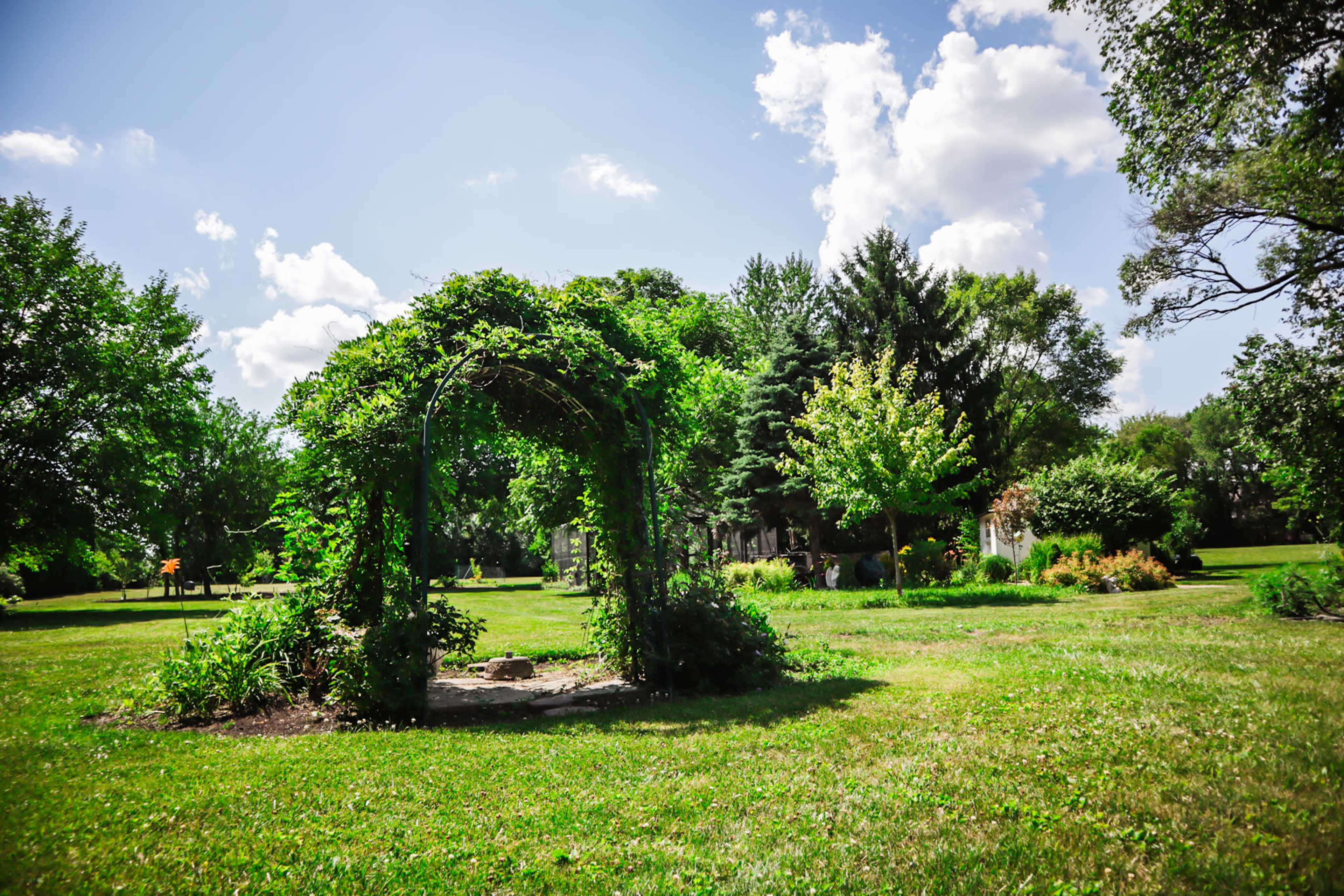 A garden gazebo surrounded by green grass and trees under a partly cloudy sky.