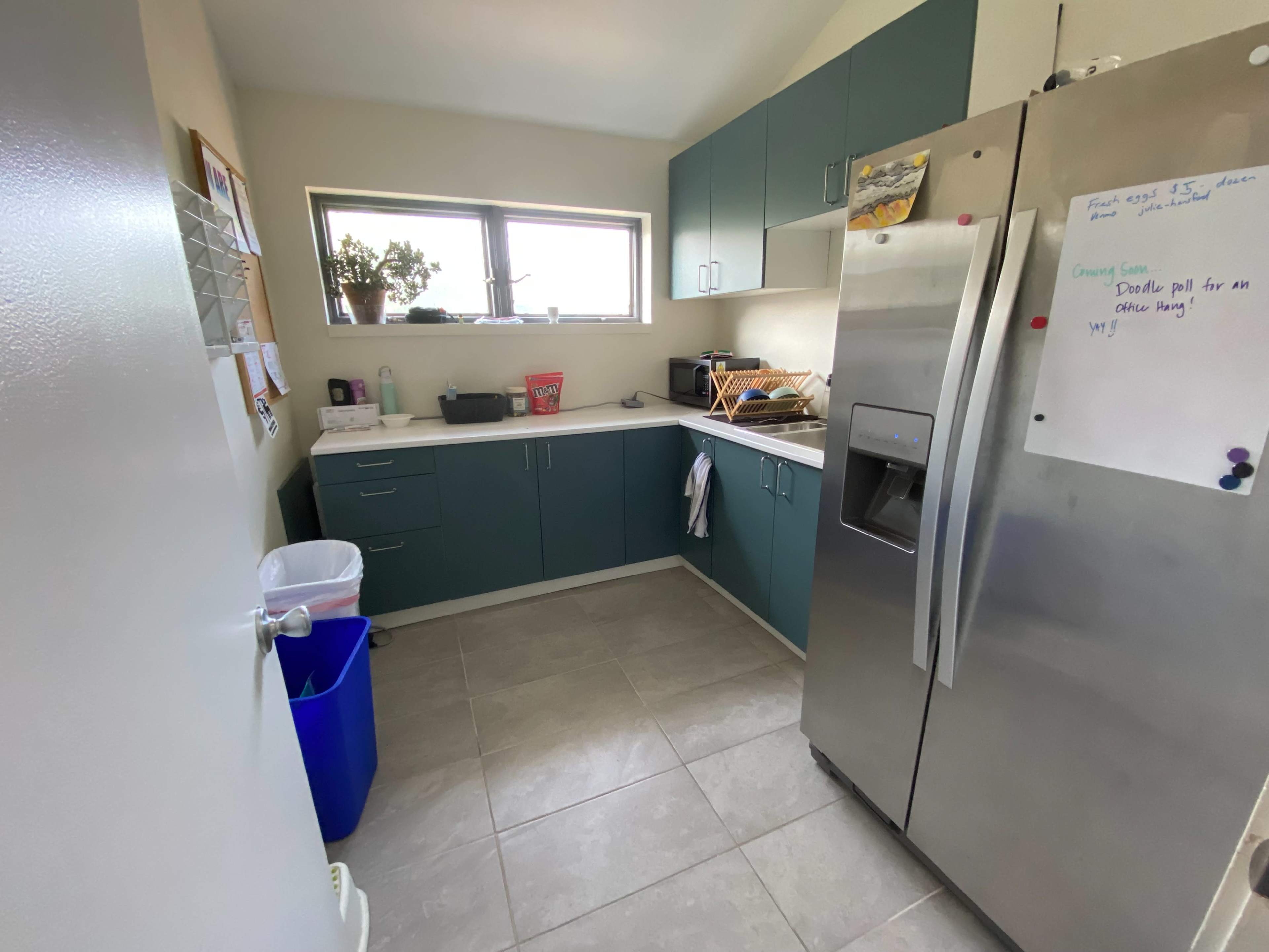 A small kitchen featuring teal cabinets, a stainless steel refrigerator, and a countertop with various kitchen items.