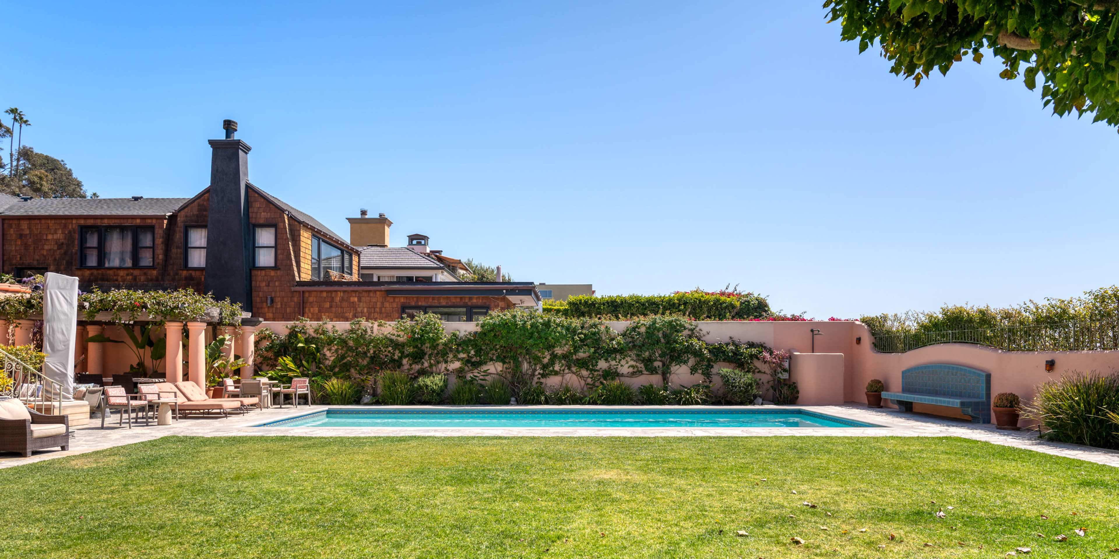 A villa with a swimming pool is surrounded by well-kept lawns and decorative landscaping under a clear blue sky.