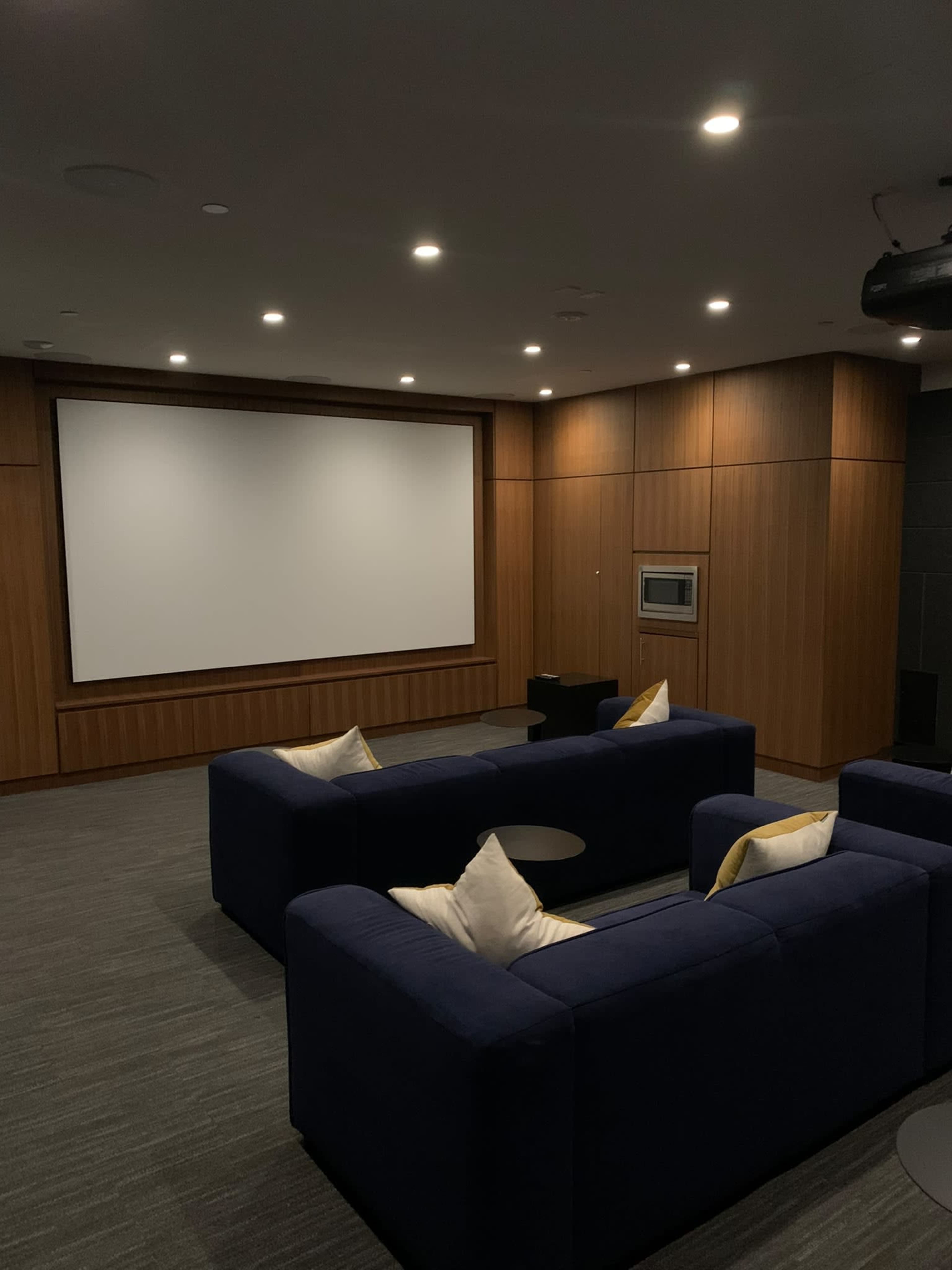 The image shows a modern home theater with blue sofas, a large screen at the front, and wood-paneled walls.